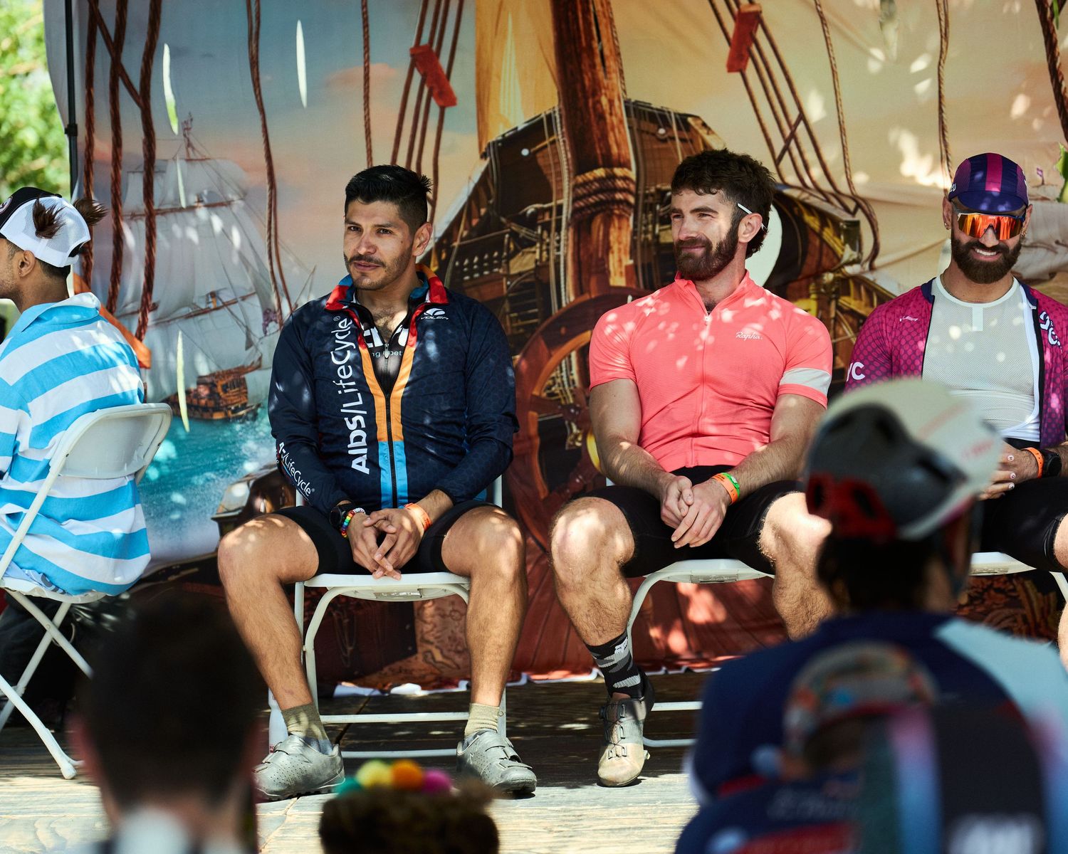 Group of cyclists relaxing under tent shade during outdoor event gathering.
