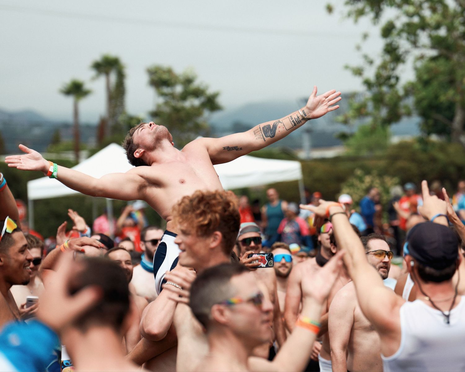 Crowd of enthusiastic spectators cheering and raising their arms during an outdoor event on a summer day.