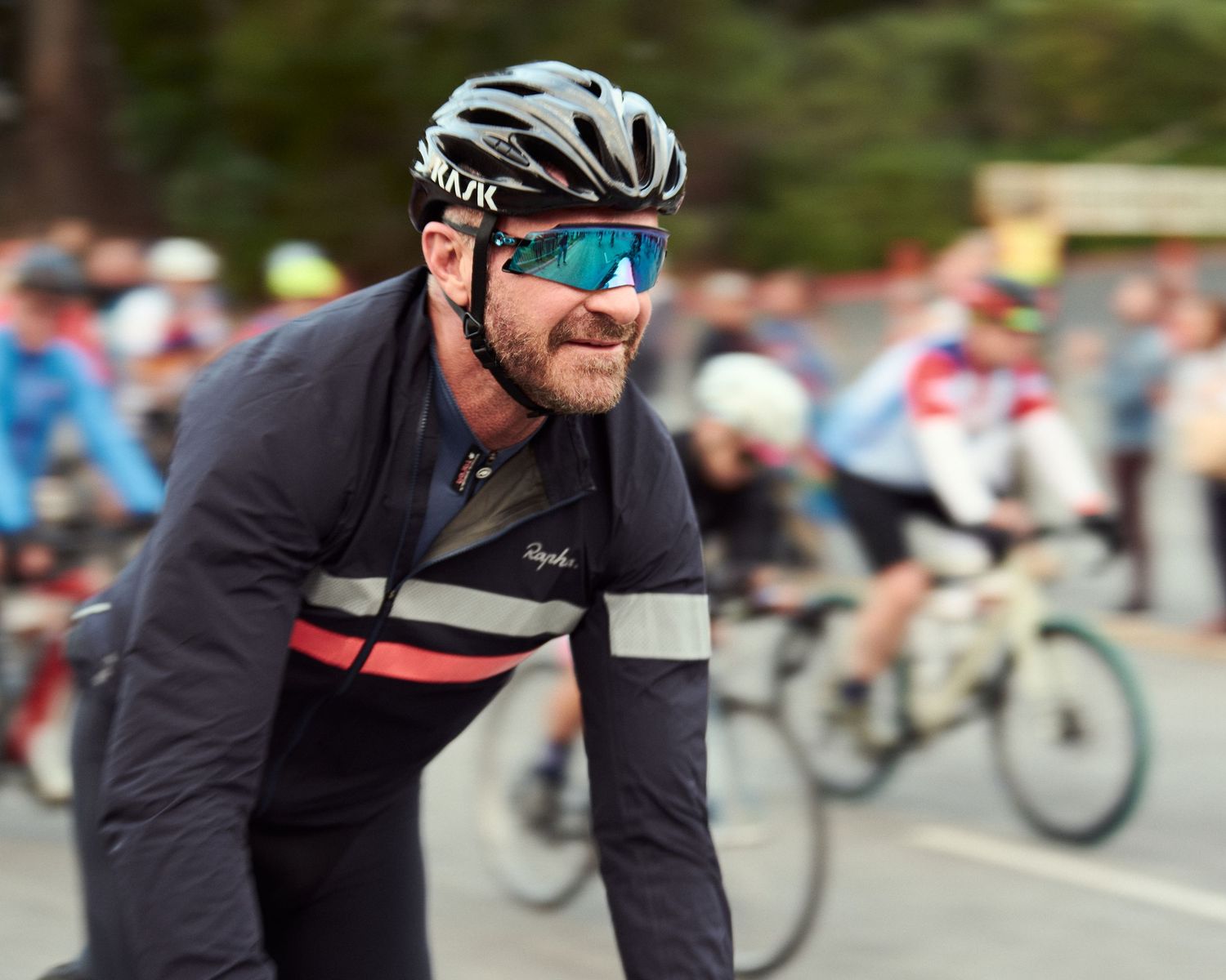 Cyclist wearing black jersey and reflective sunglasses participates in organized cycling event.