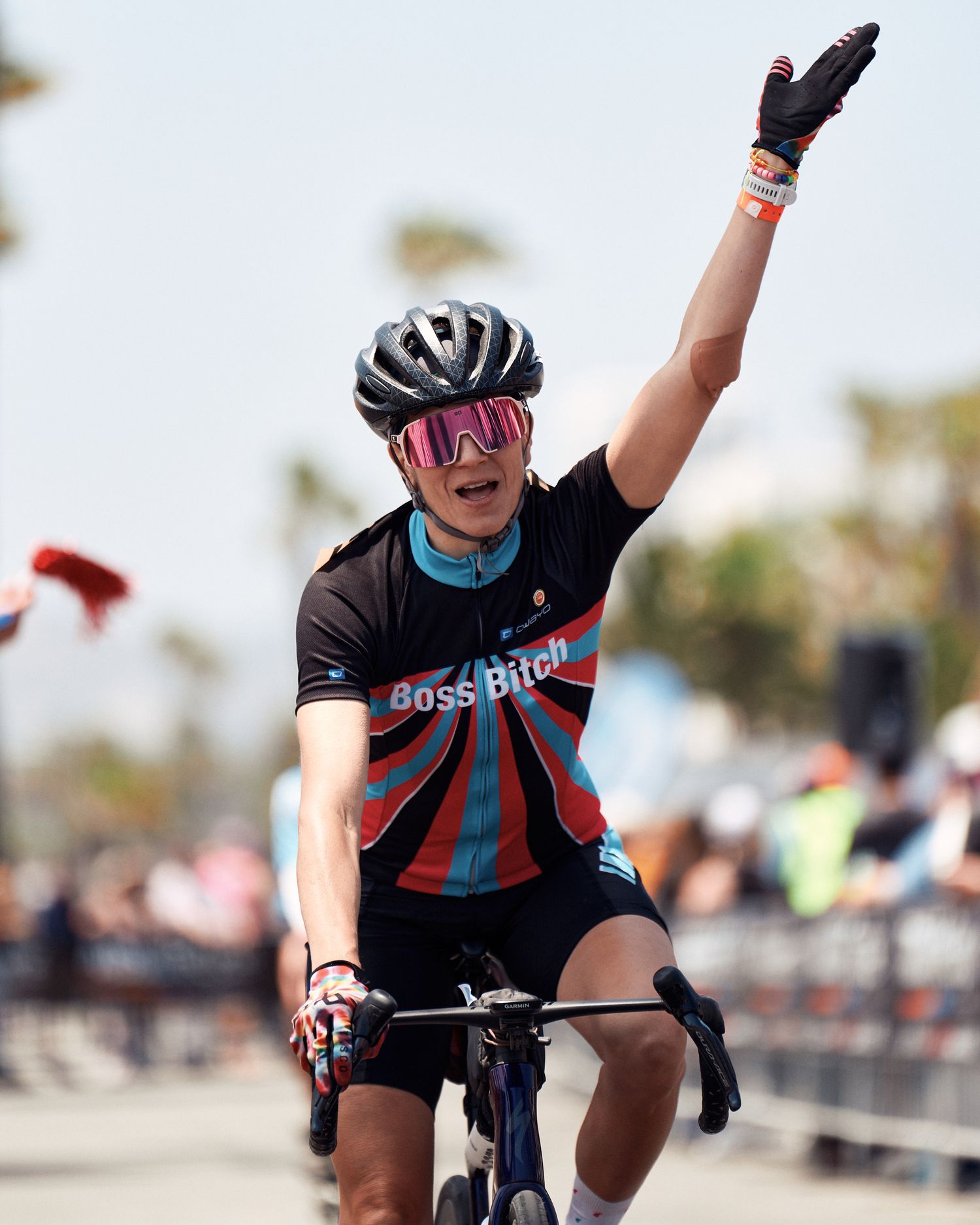Cyclist in black jersey and cycling helmet raises arm in victory gesture during outdoor cycling event.