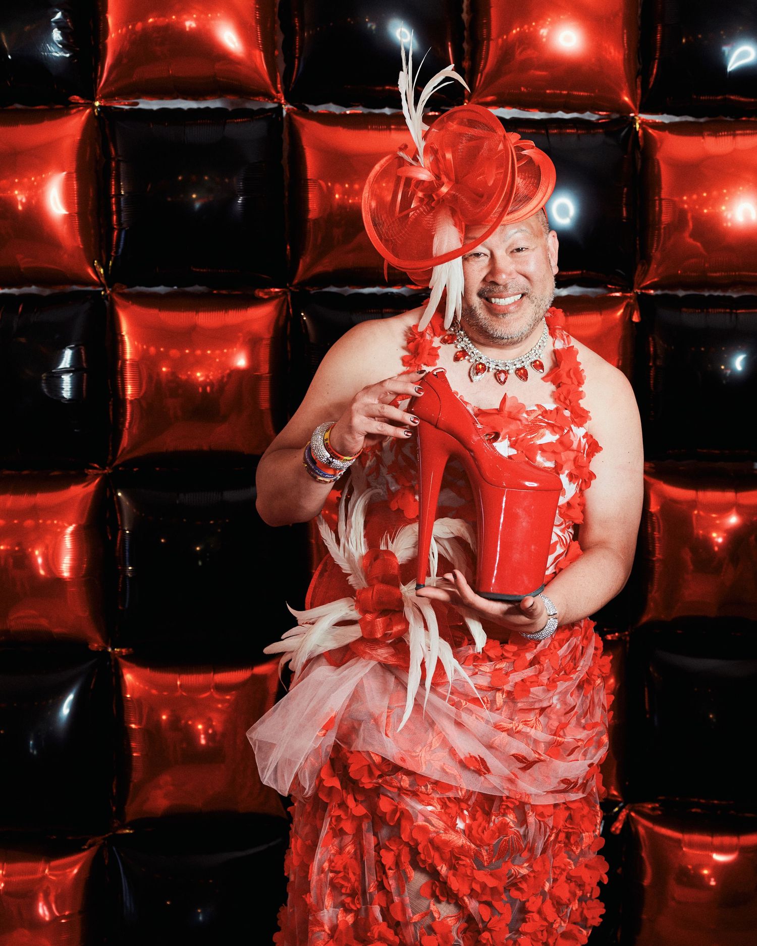 A performer wearing a red and white tulle dress costume performs under dramatic red lighting on a dark stage.