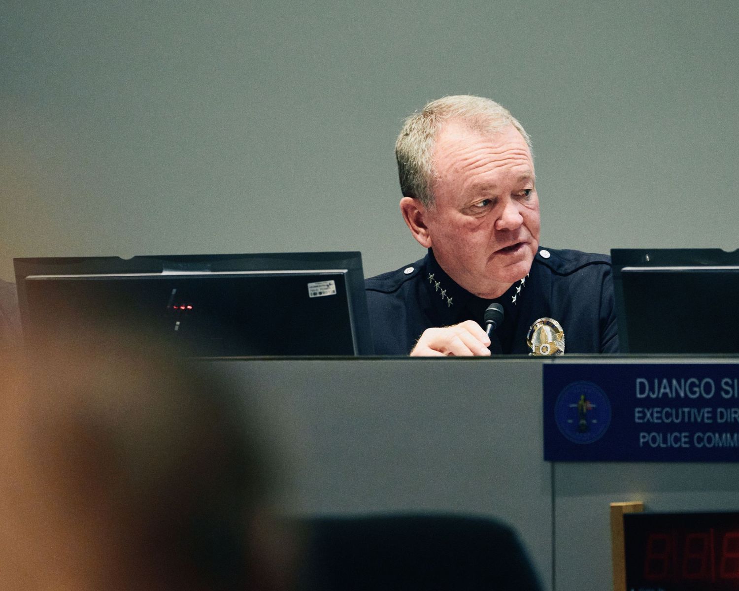 Police commissioner Django sits at a desk with monitors during an executive committee meeting.
