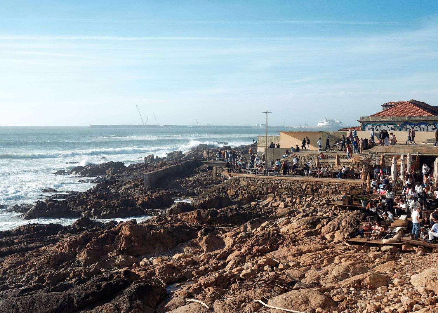 Tourists gather along the rocky coastal cliffs to watch dramatic ocean waves crash against the rugged shoreline.