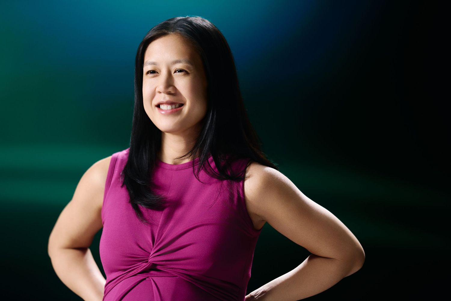 Professional portrait of someone wearing a sleeveless magenta top against a dark green and blue background.