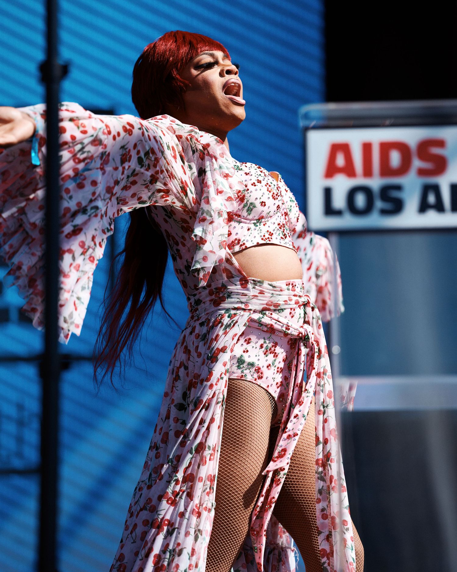 A person in a floral dress twirls and dances against a blue background with text signage visible.