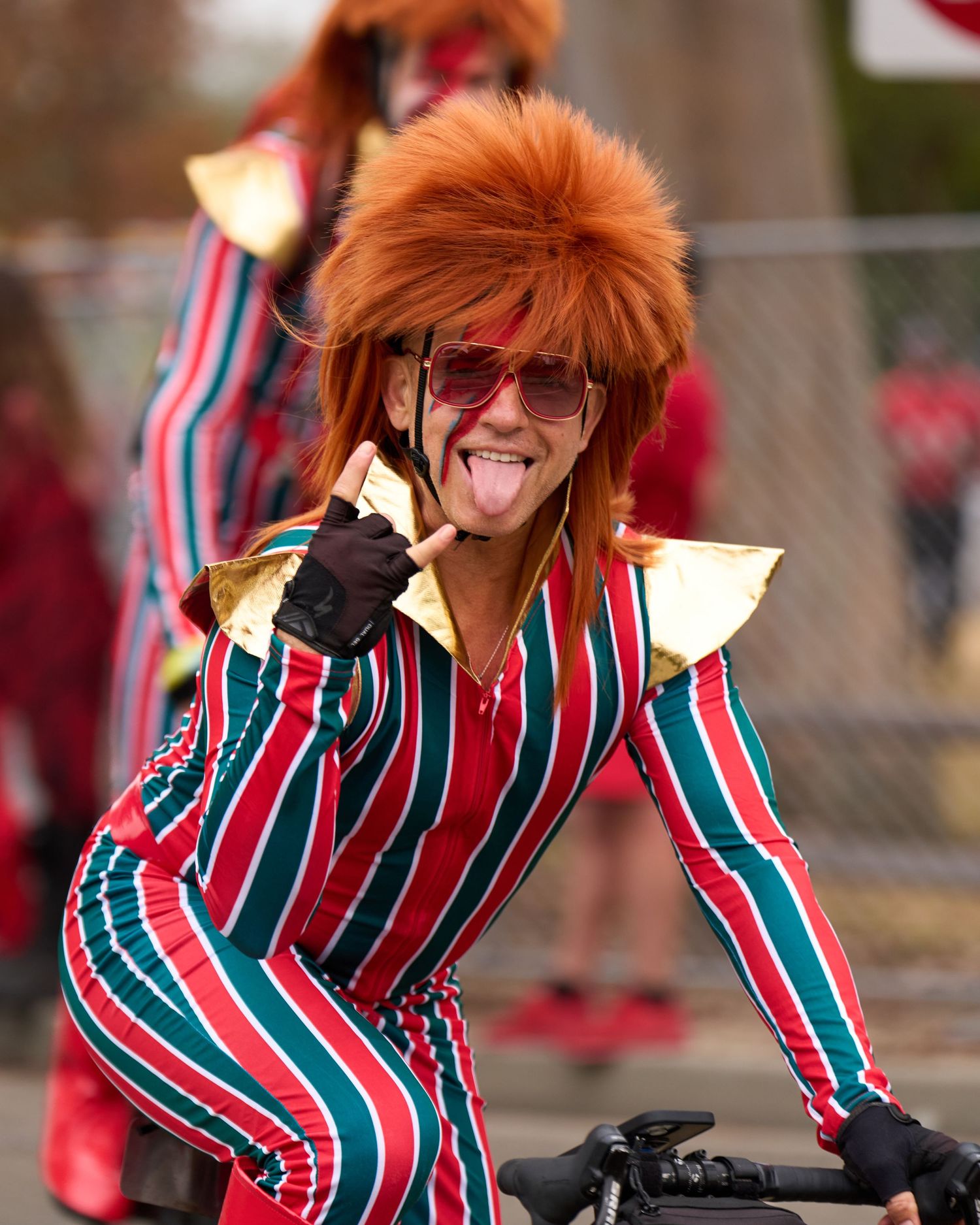 Person in red and green striped outfit and bright orange hair dancing energetically during a celebration event.