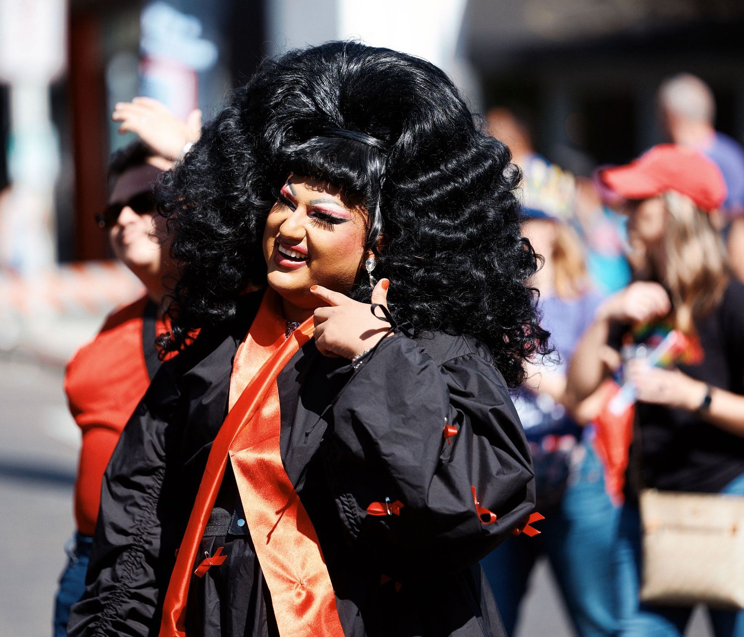 A person with dark curly hair wearing black clothing performs on stage with expressive gestures and movements.