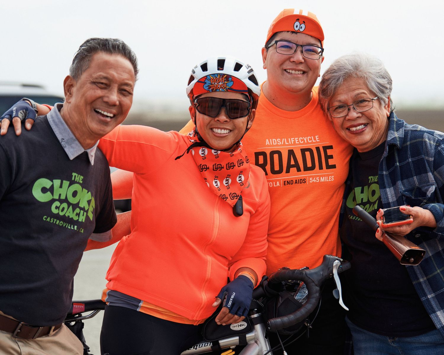 Group of cyclists in orange jerseys pose together for a photo outdoors.