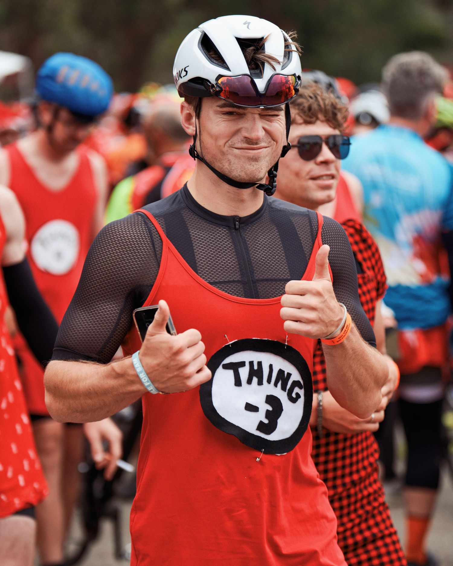Participant in a cycling event wearing a red jersey and helmet giving thumbs up.