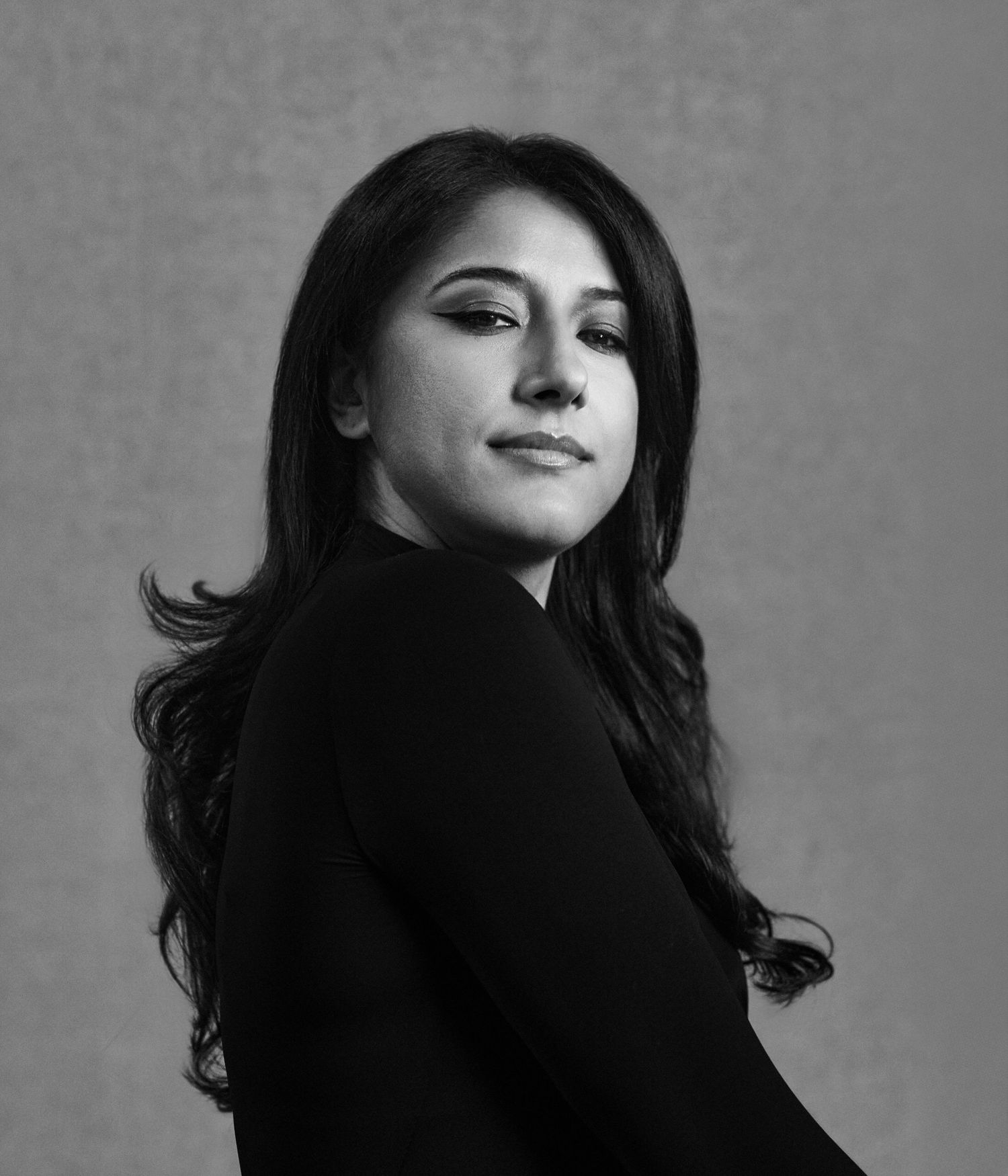 Black and white portrait of a woman in dark turtleneck sweater with flowing dark hair against a plain background.