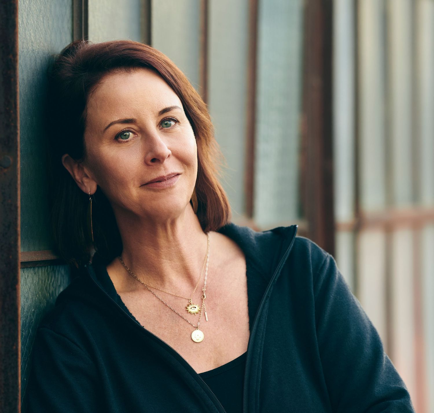Person in a black top smiling warmly while posing against a window in natural lighting.