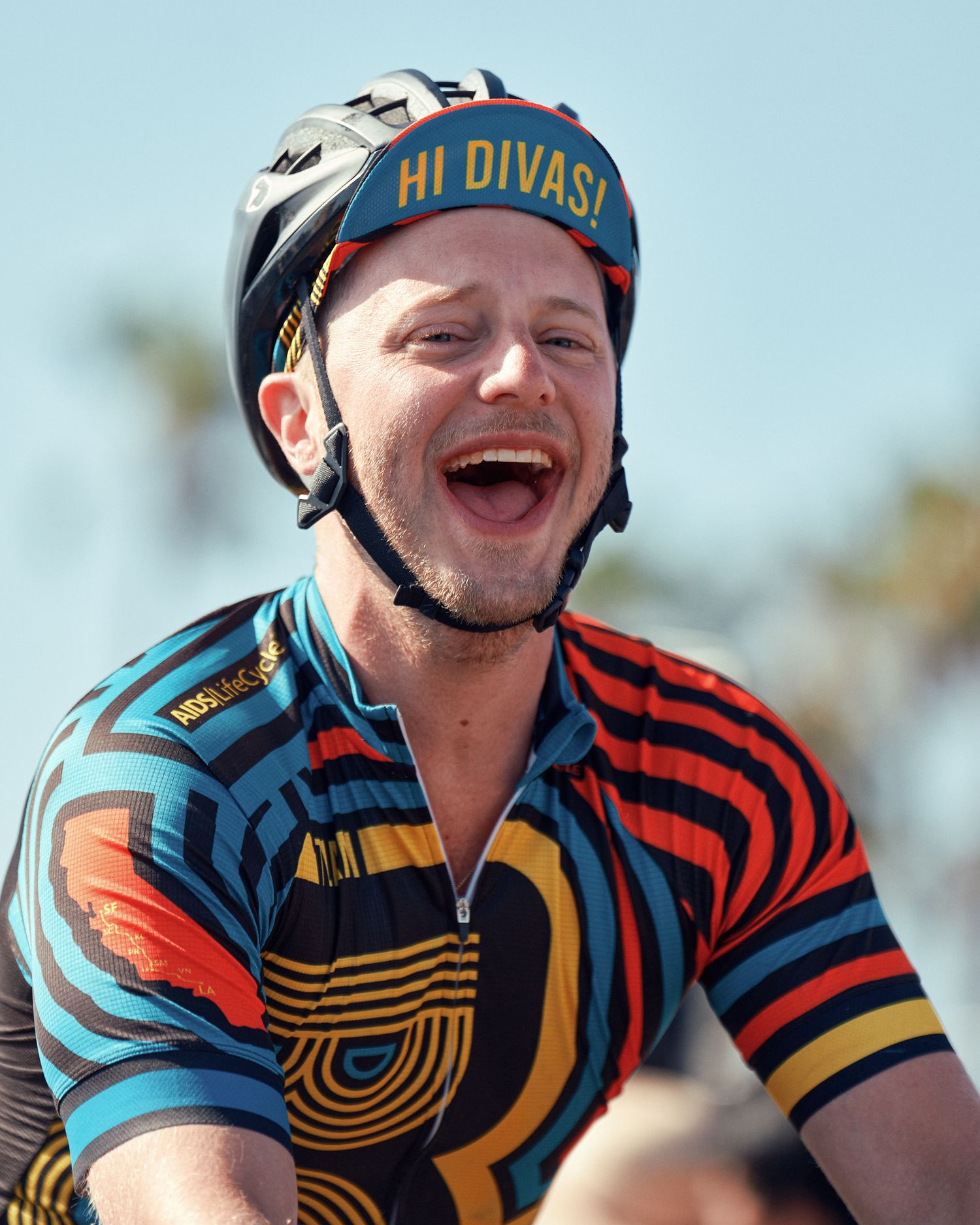 Athletes wearing colorful patterned cycling jerseys smile and laugh during an outdoor event.