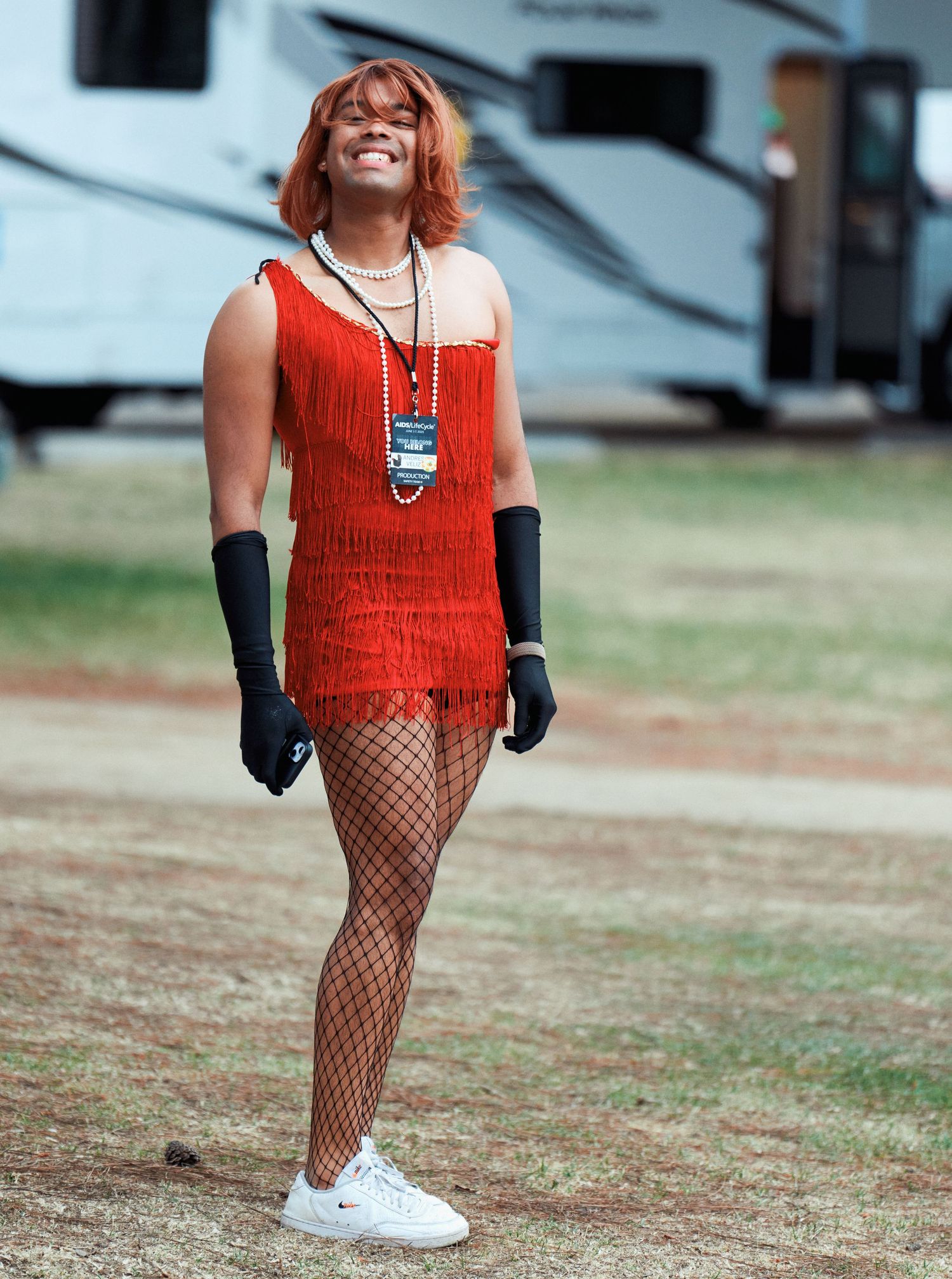 Person wearing a bright red flapper-style dress with fishnet stockings and white sneakers stands outdoors.