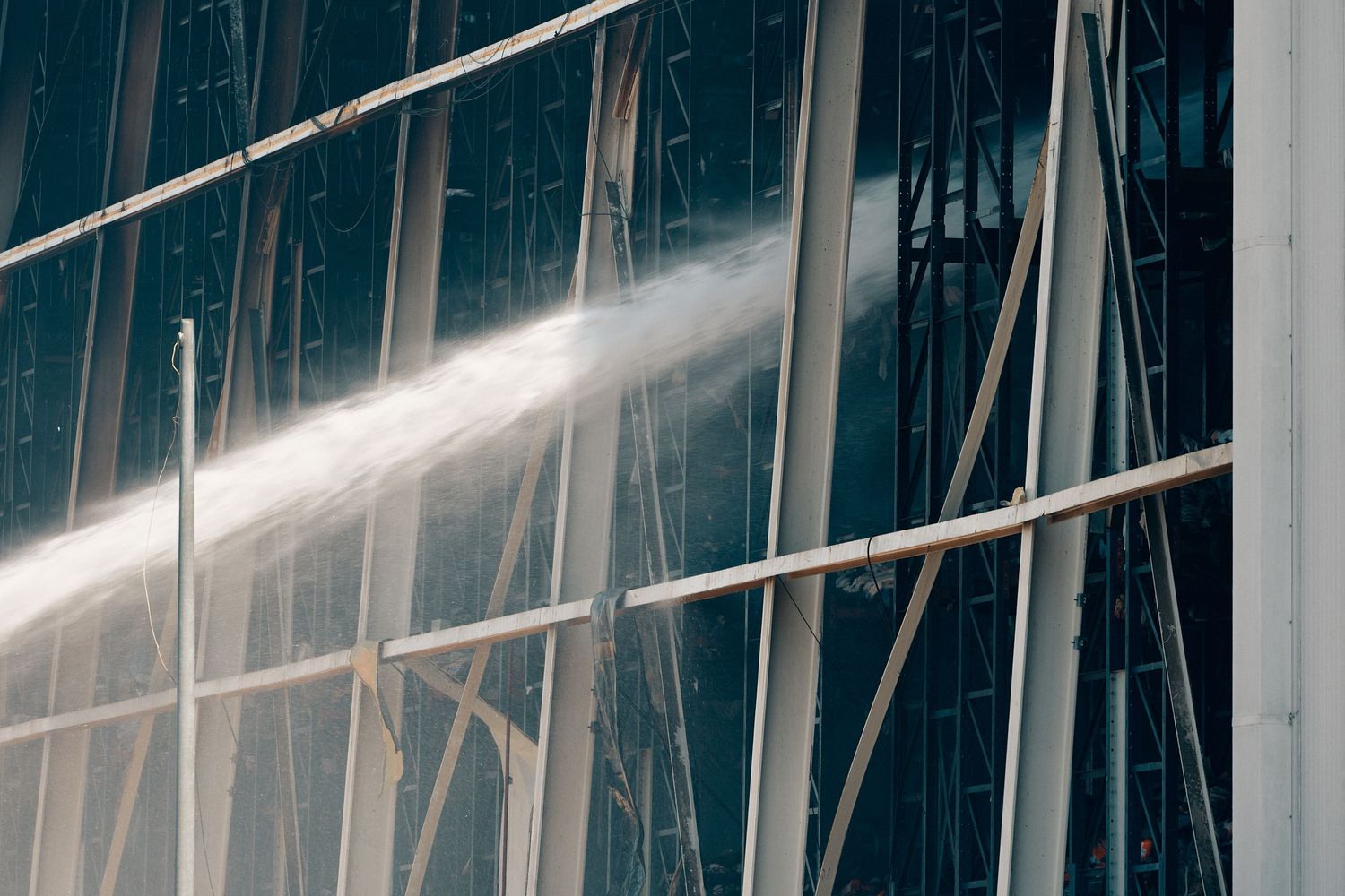 Water jet spraying against a modern glass and steel building facade during firefighting or cleaning operations.