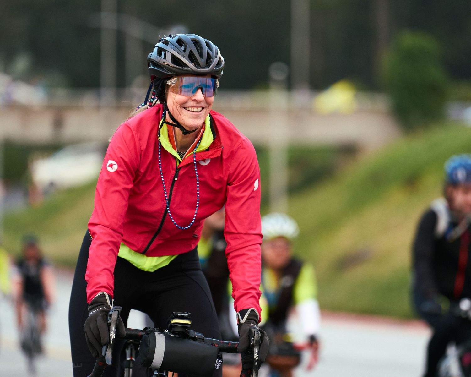 Cyclist wearing red jacket and helmet smiles while riding during outdoor cycling event.