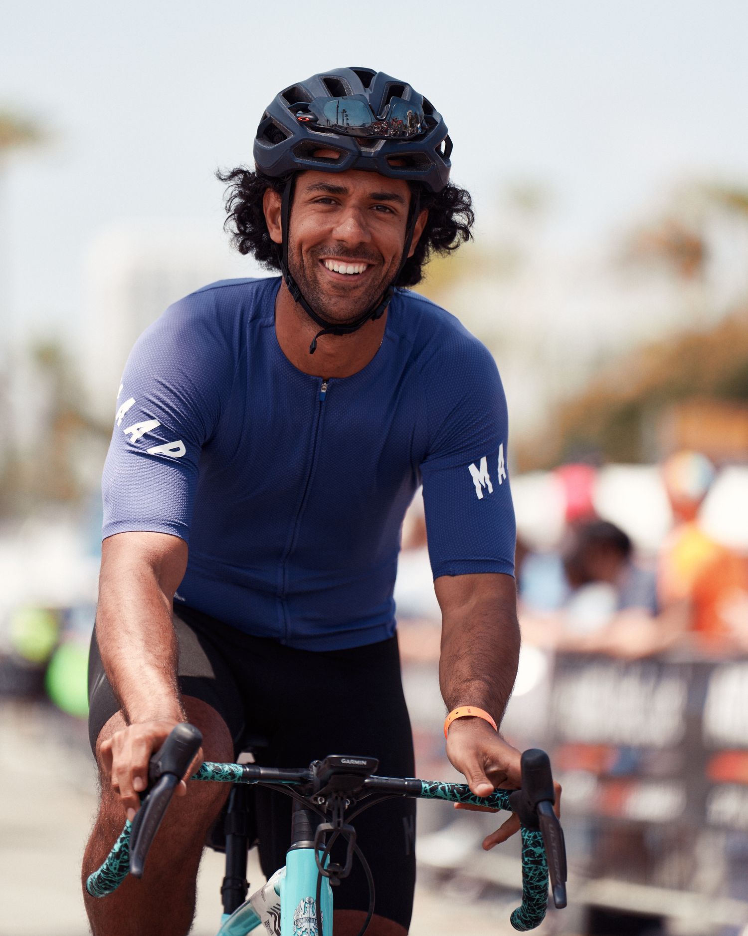 Cyclist wearing navy cycling jersey and black helmet rides turquoise bike during outdoor event.