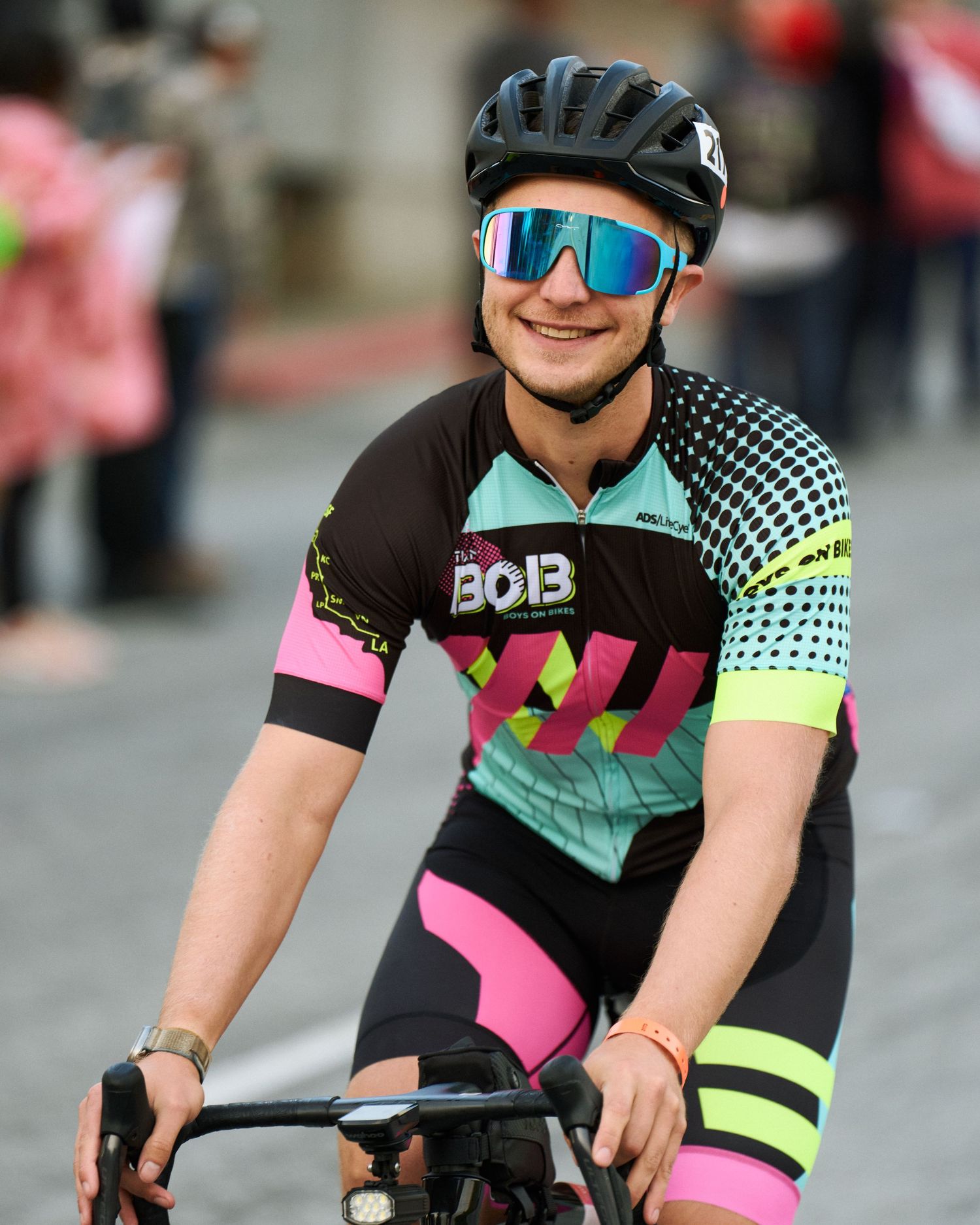Cyclist wearing colorful black, pink and mint cycling jersey with reflective sunglasses and helmet on city street.