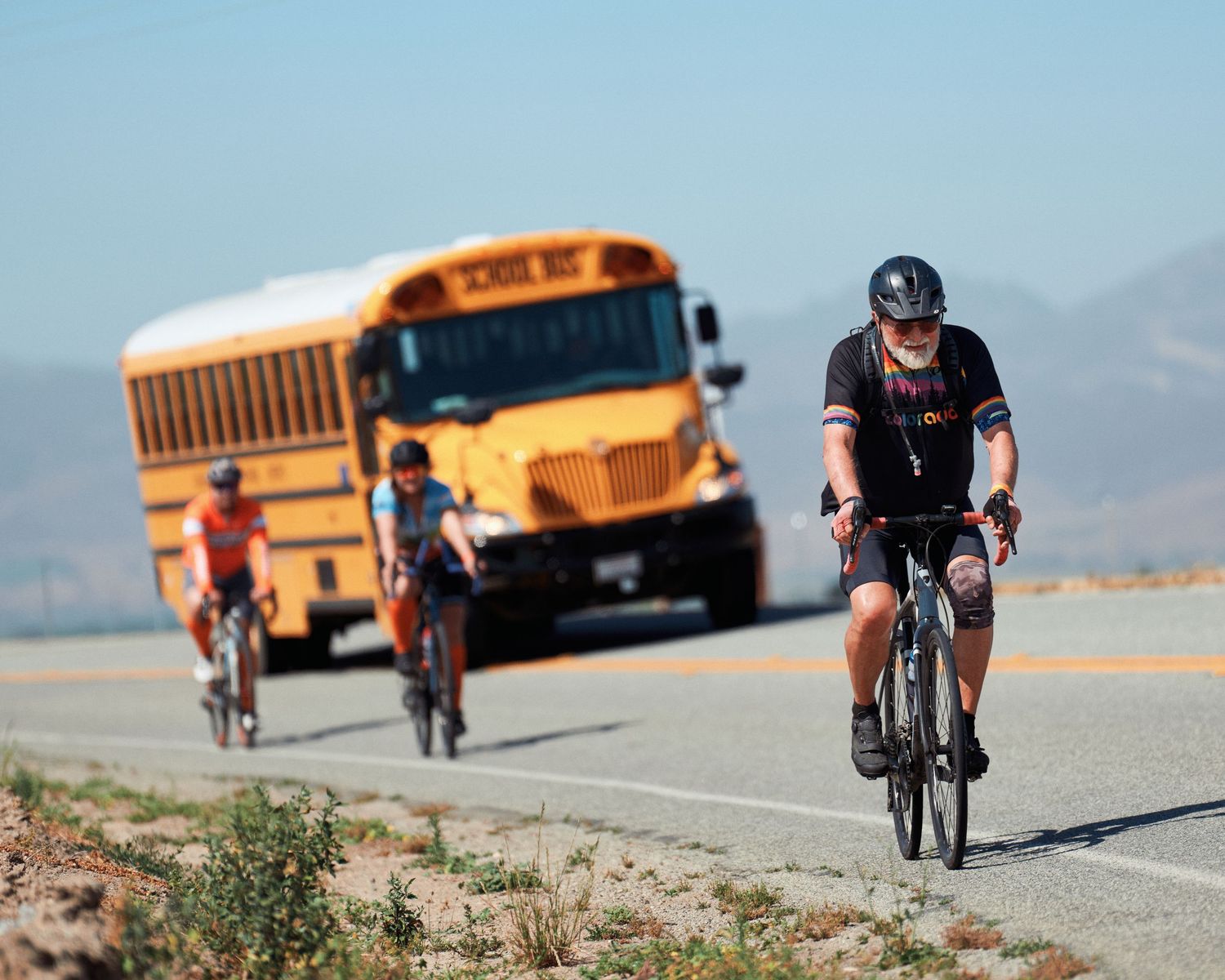 Cyclists riding on rural road with yellow school bus in background.