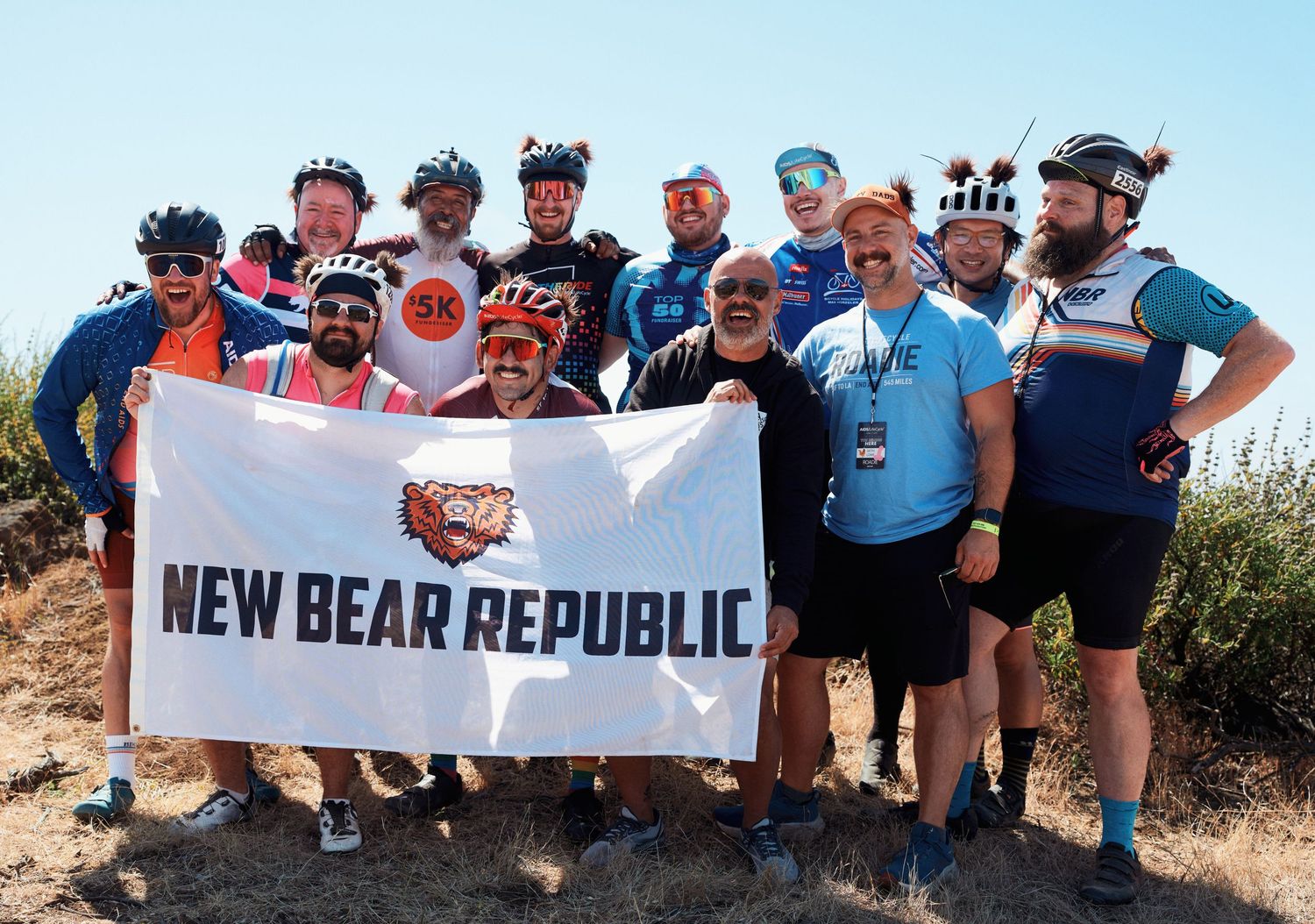 Group of cyclists holding 'New Bear Republic' banner during an outdoor cycling event.