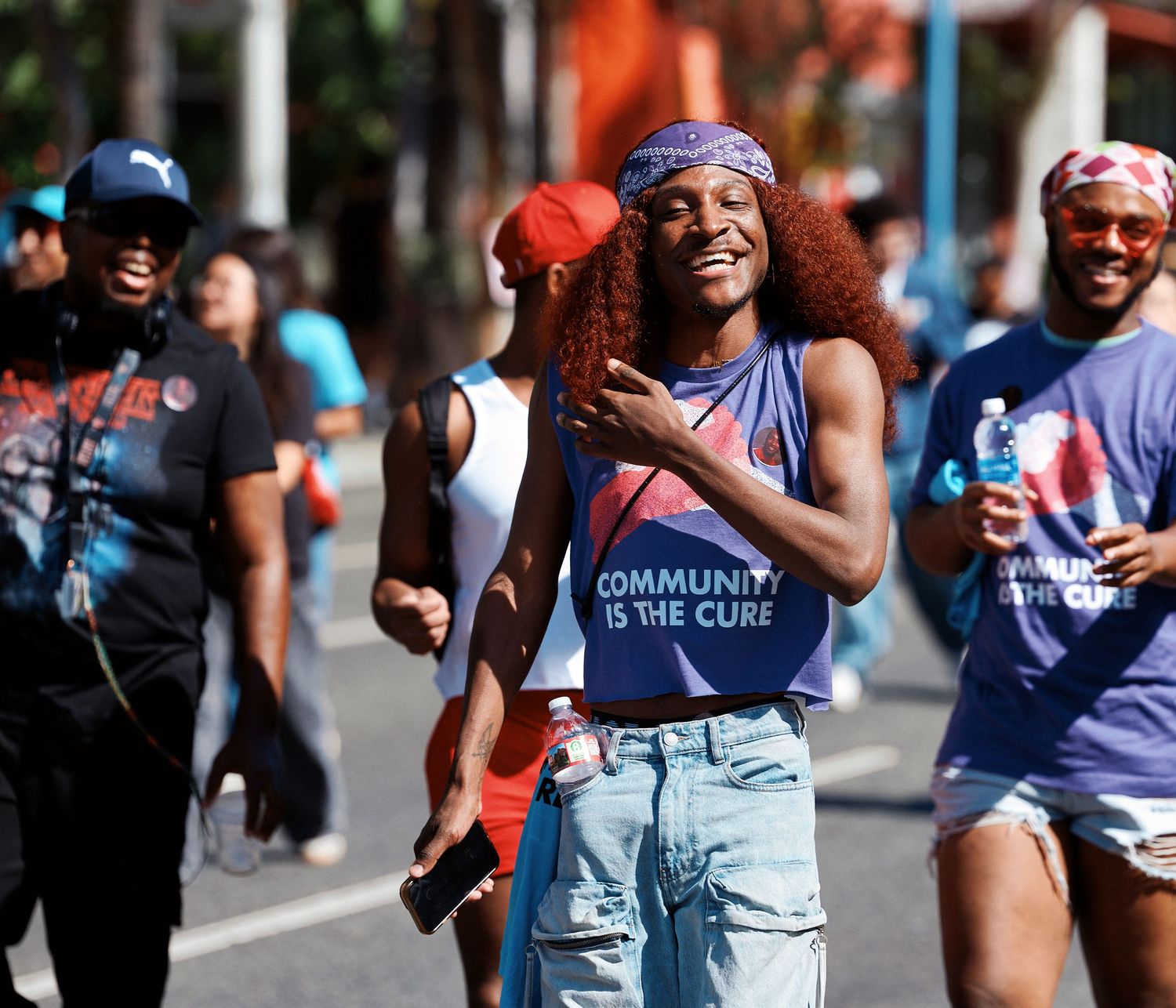 Participants celebrate and cheer while running in an outdoor community marathon event on a sunny day.
