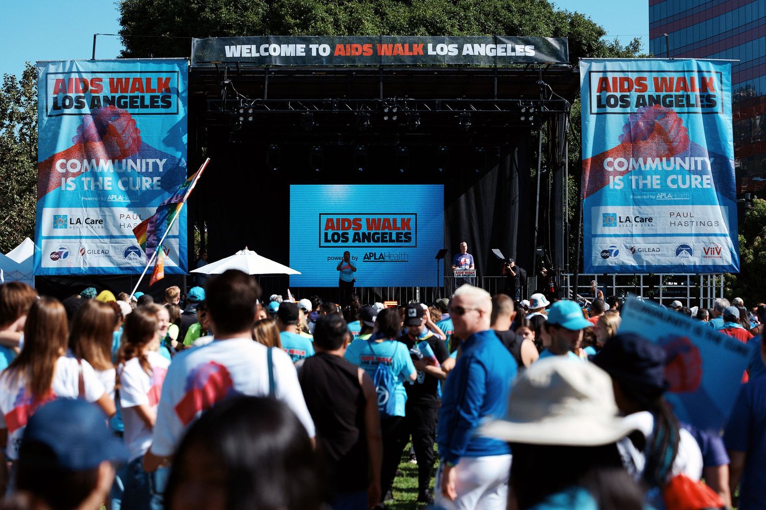 Large crowd gathers in front of outdoor concert stage with blue banners and screens at Los Angeles fan event.