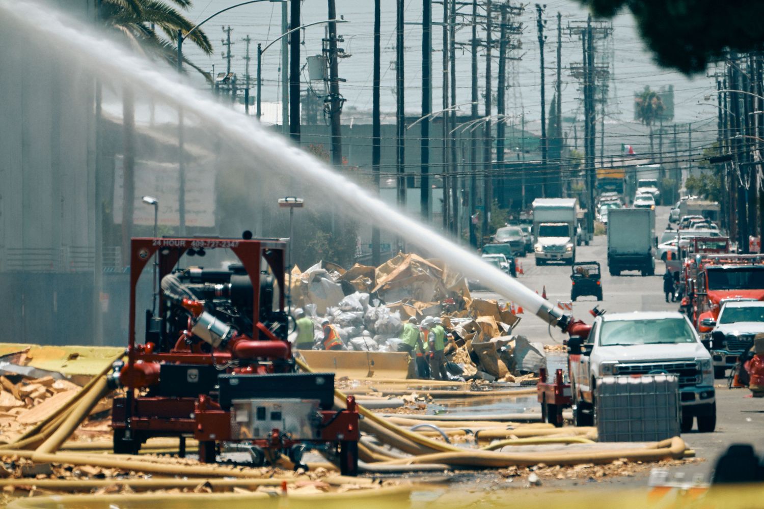 Emergency crews use water cannons at a debris-filled construction site explosion on a busy urban street.