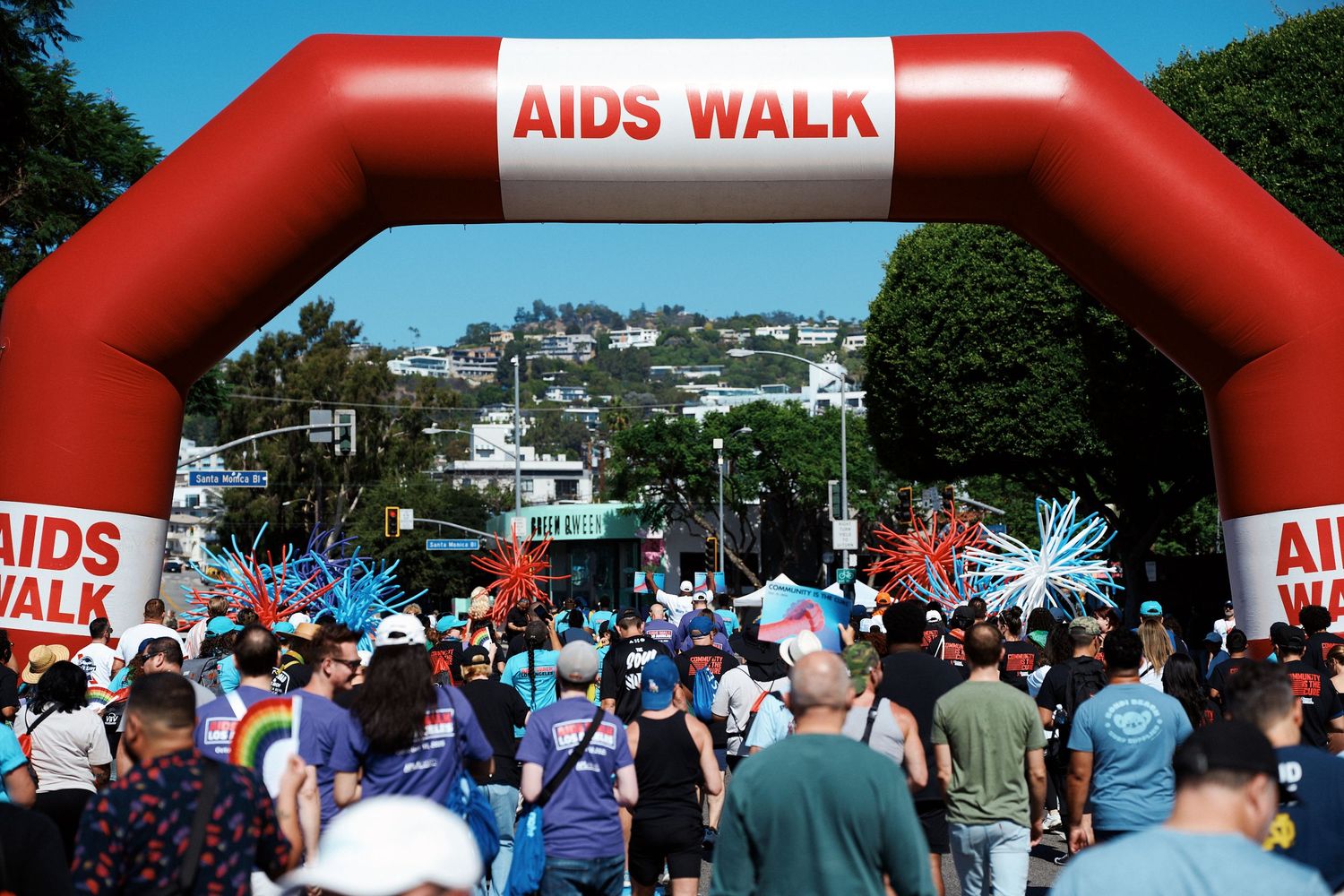 Participants gather under a large red inflatable arch at an AIDS Walk fundraising event on a sunny day.