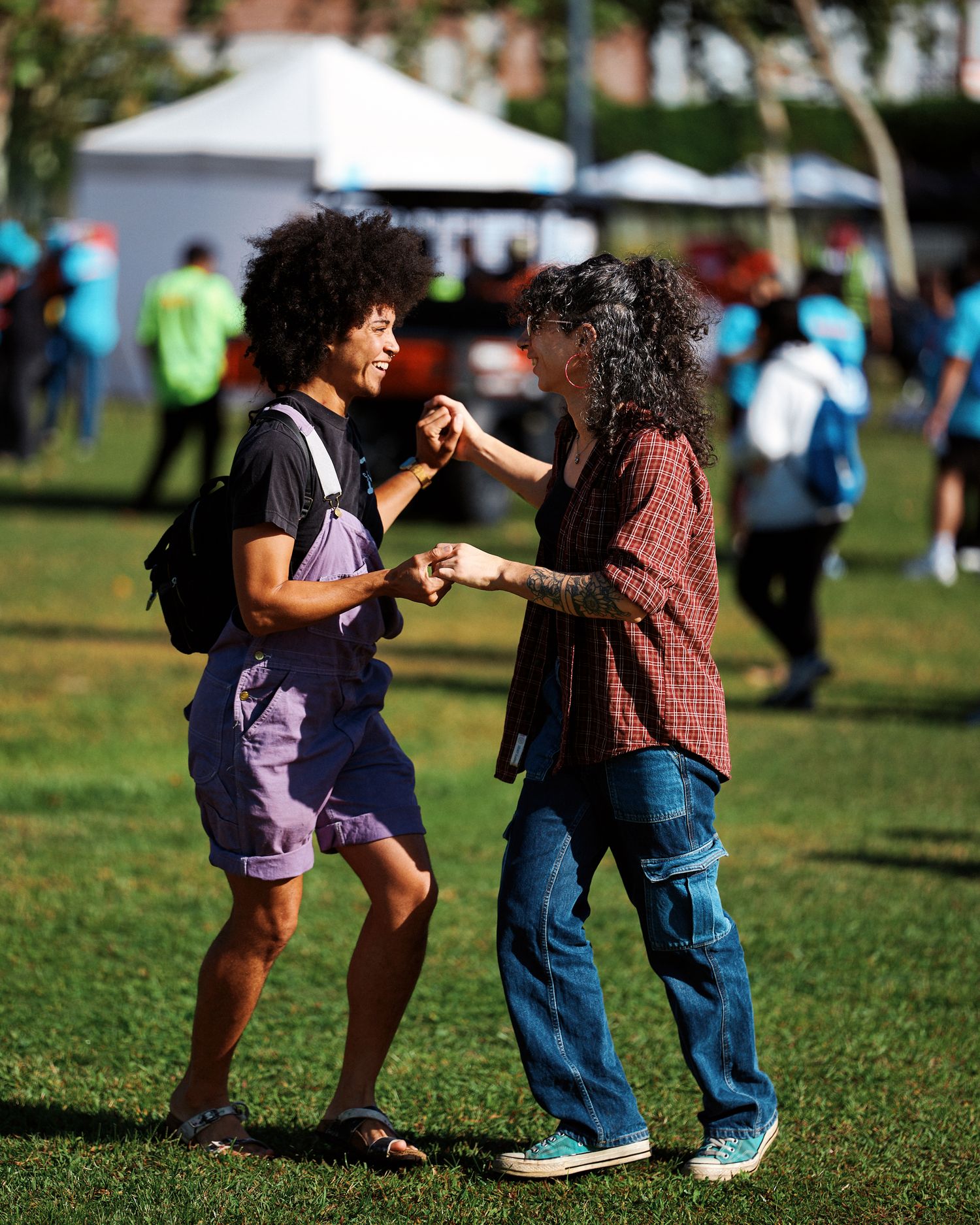 People dancing together on a grassy lawn at an outdoor gathering with tents visible in the background.