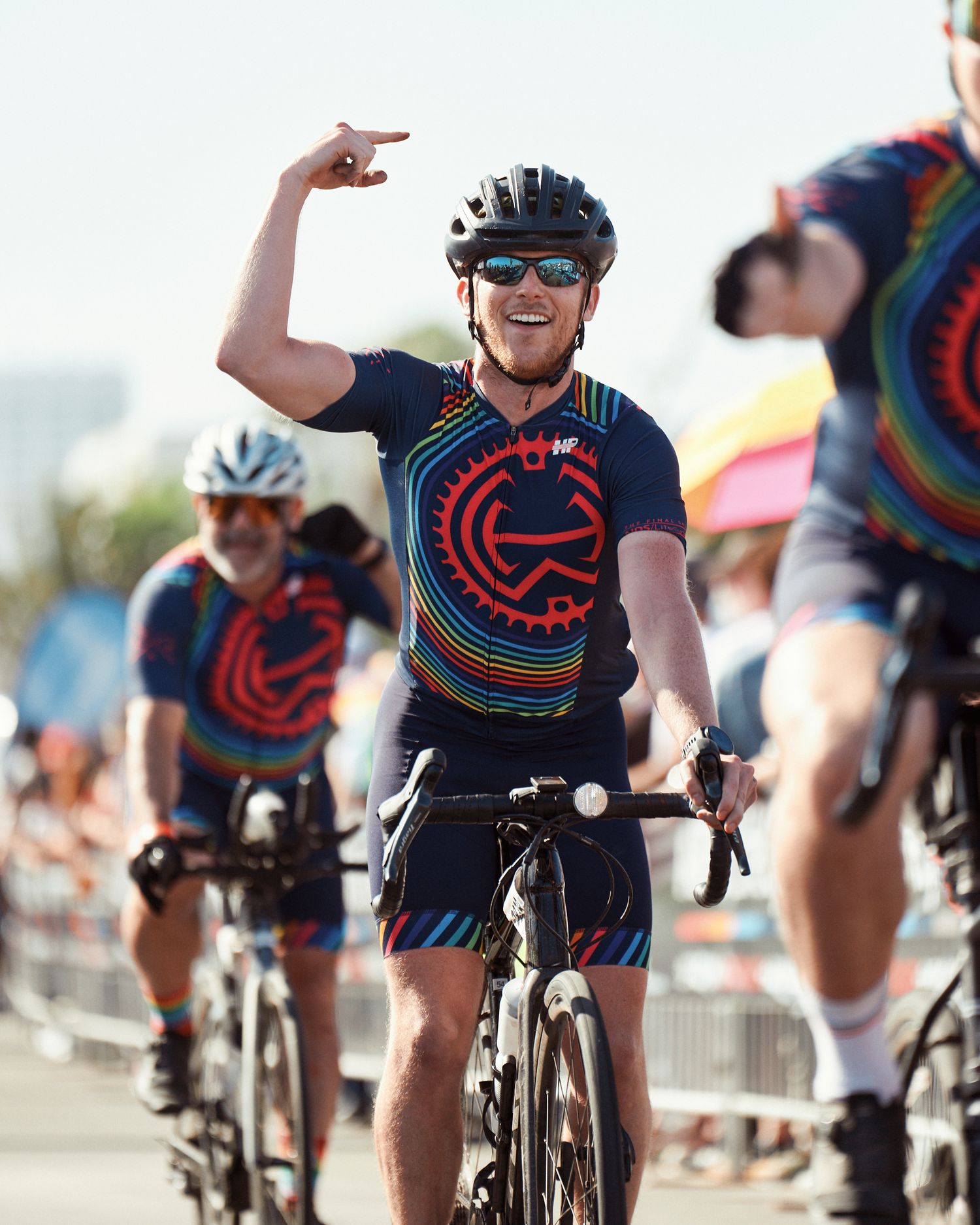 Cyclist in navy blue and red jersey celebrates while riding during an outdoor cycling event on a sunny day.