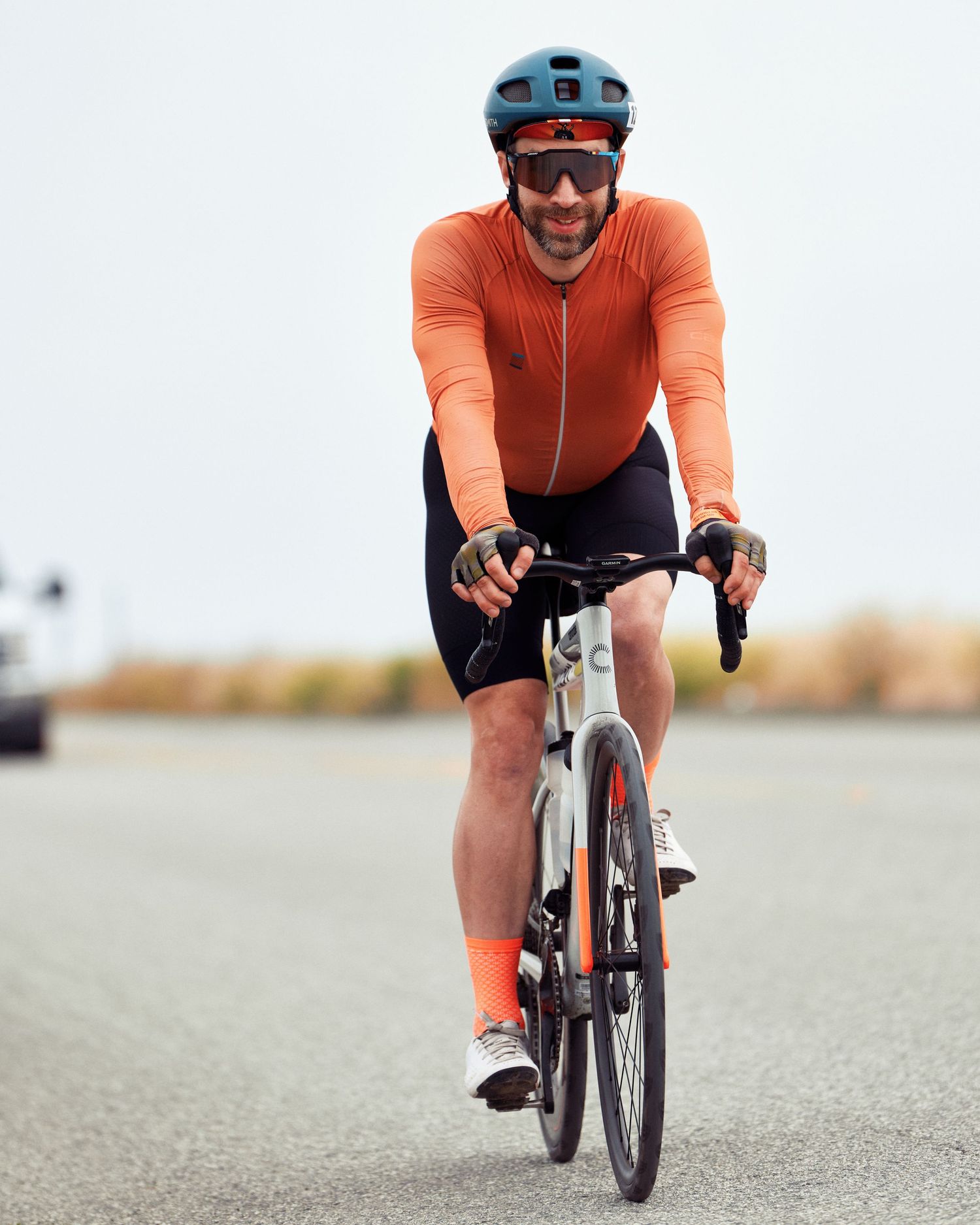 Road cyclist in bright orange jersey and black shorts rides bike on open road.