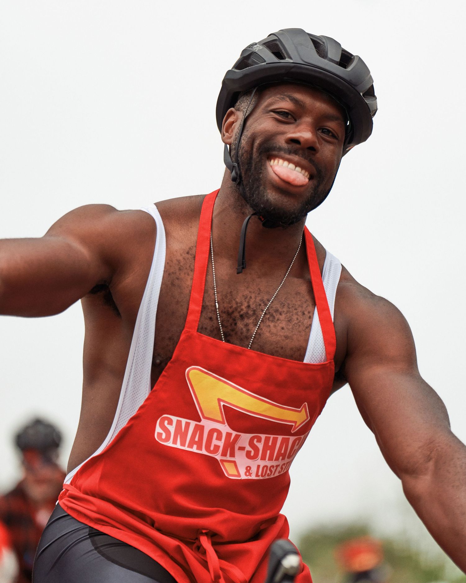 Cyclist wearing red tank top and helmet smiles during outdoor cycling event.