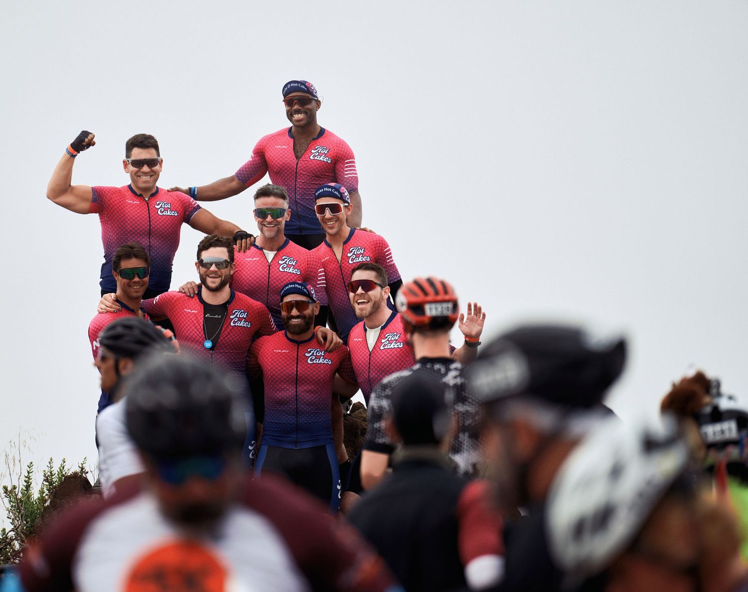 Group of cyclists in matching red jerseys celebrating together during an outdoor event.