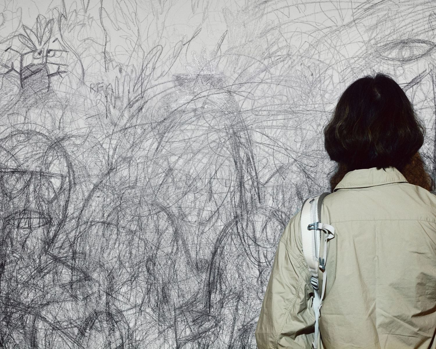 A visitor stands before a wall of overlapping charcoal shadow outlines in Yoko Ono’s Shadow Piece at The Broad.