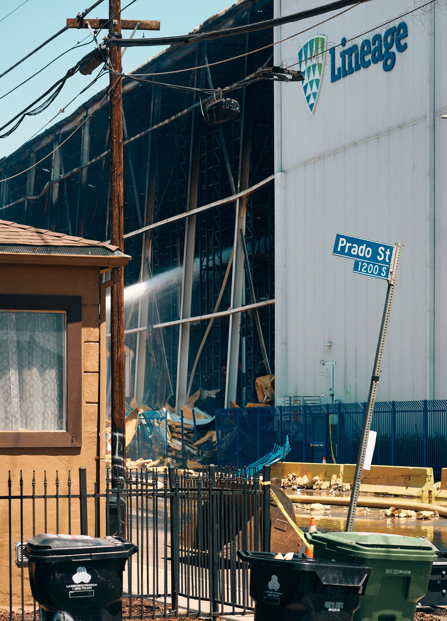 Lineage cold storage facility fire damage on Prado St, with water stream visible and debris scattered near residential area.