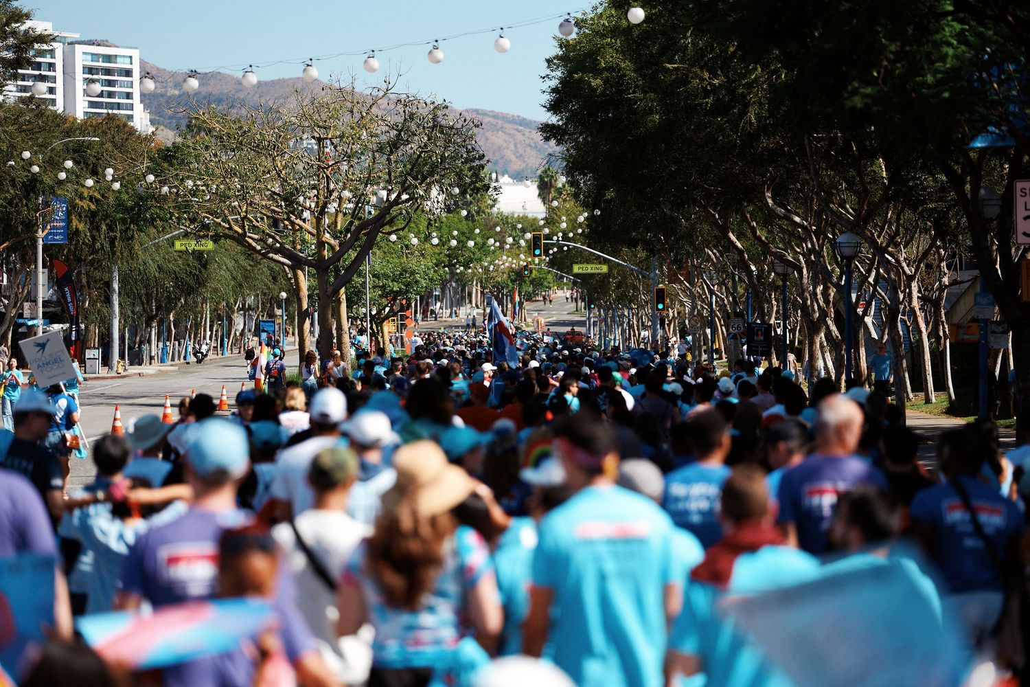 Large crowd of people wearing light blue shirts gathered outdoors at a public event or rally.