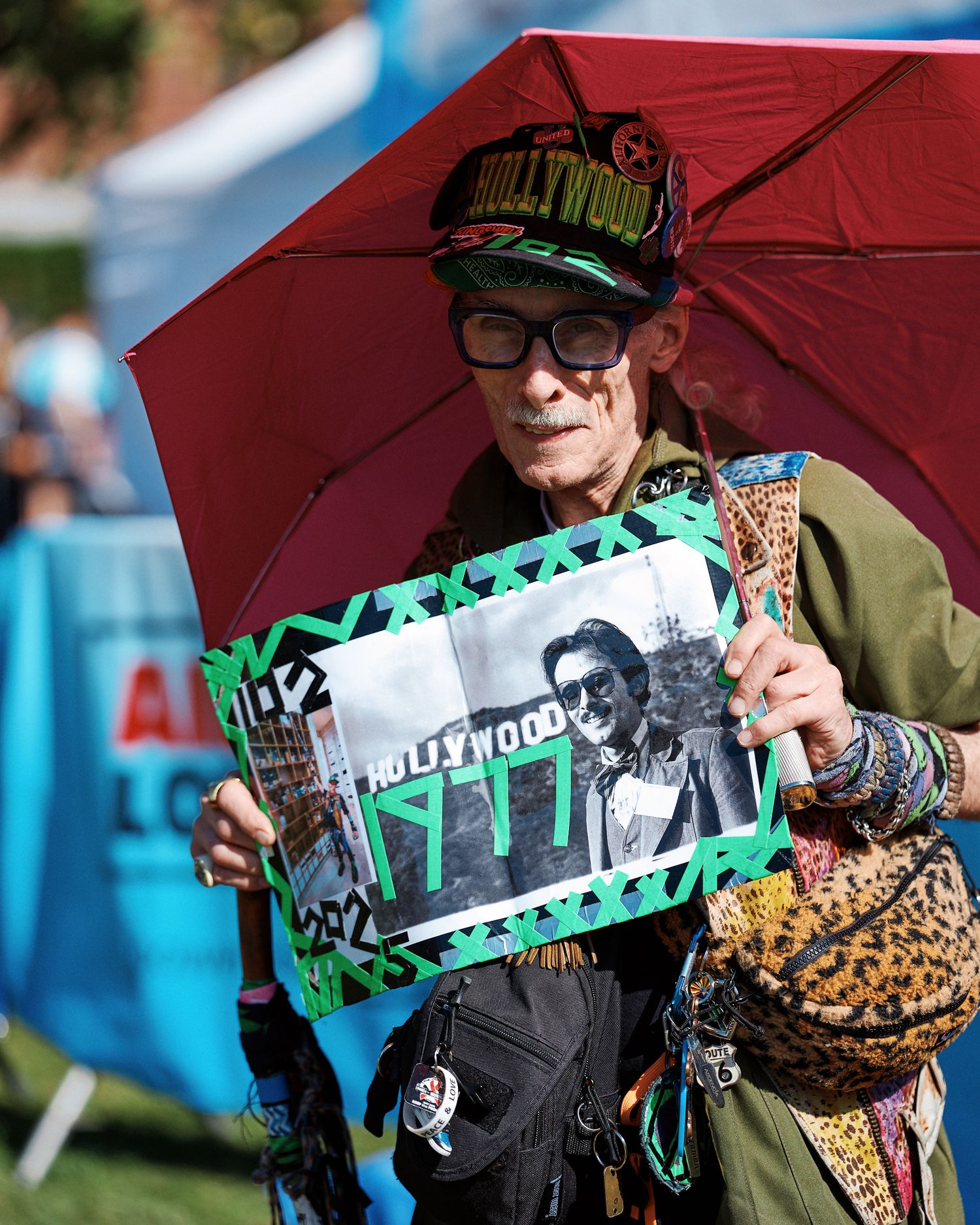 Music fans hold up U2 band memorabilia under red umbrellas at an outdoor event.