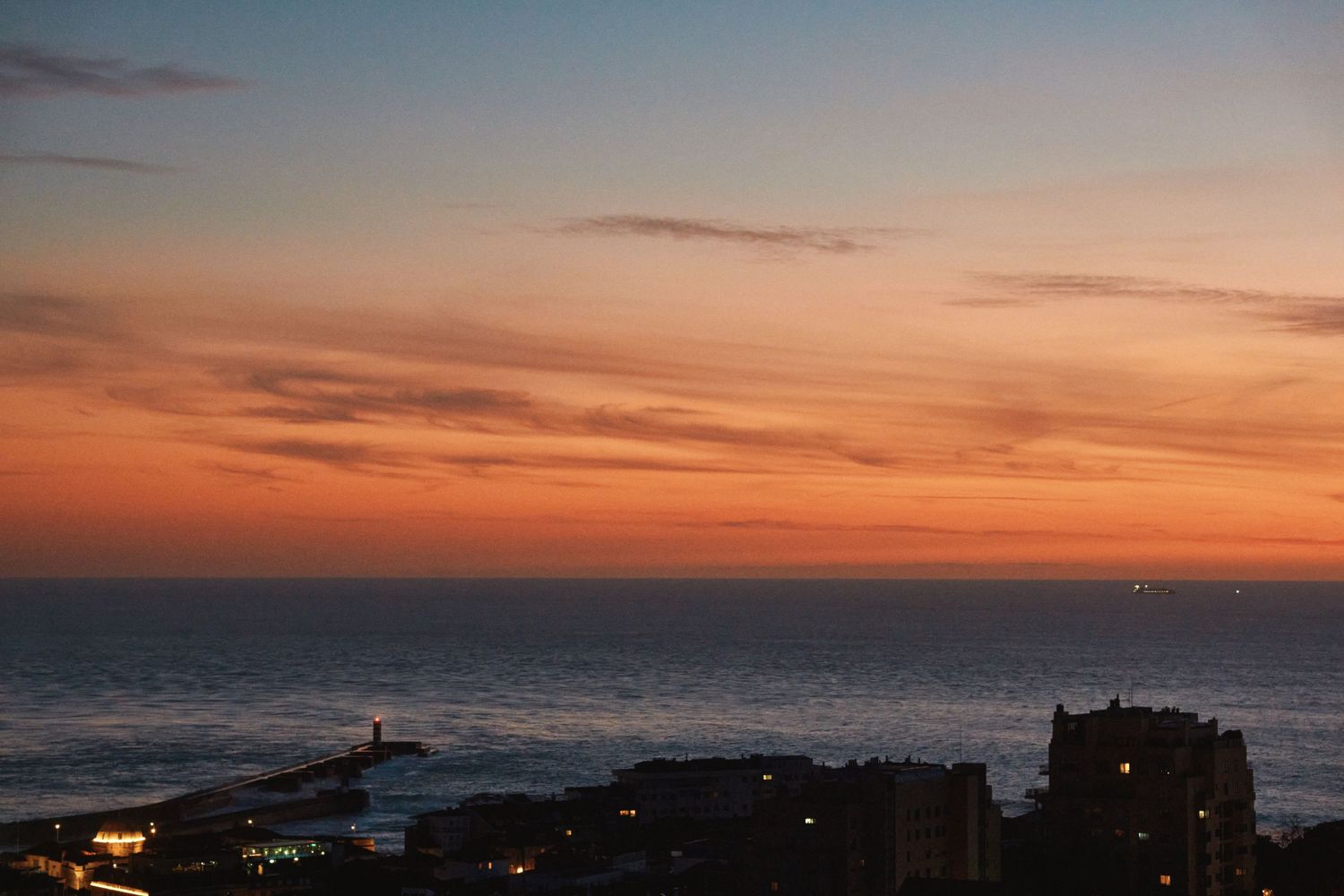 Panoramic sunset view over the ocean with vibrant orange and pink clouds reflecting on the calm water's surface.