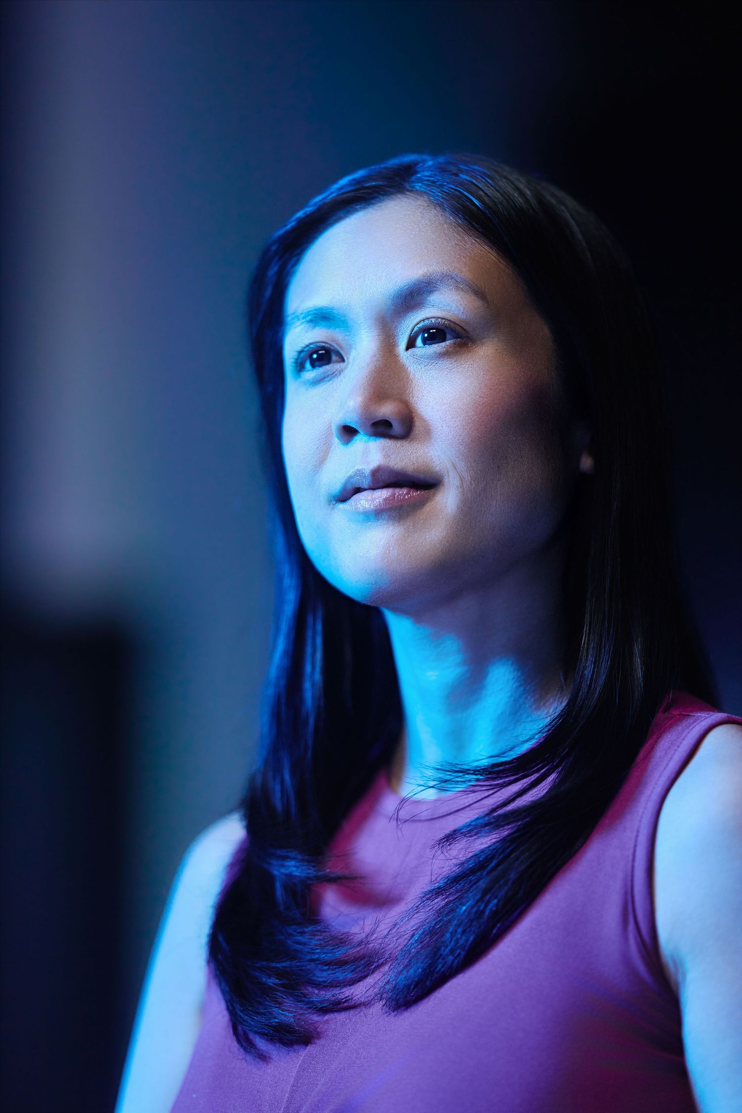 Portrait with moody blue lighting illuminating subject wearing purple tank top as they gaze upward contemplatively.