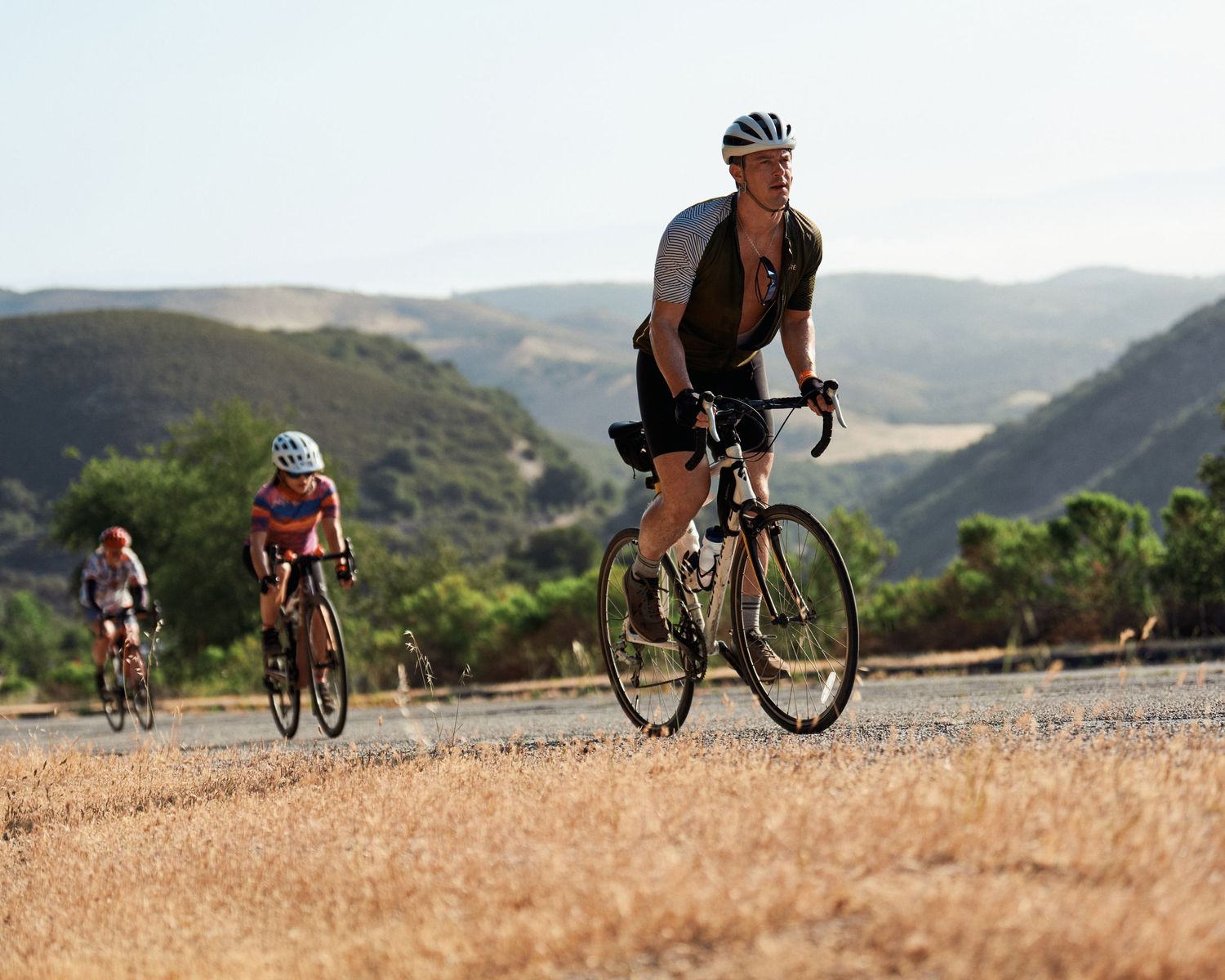 Cyclists riding road bikes on a scenic mountain trail during a sunny summer day.
