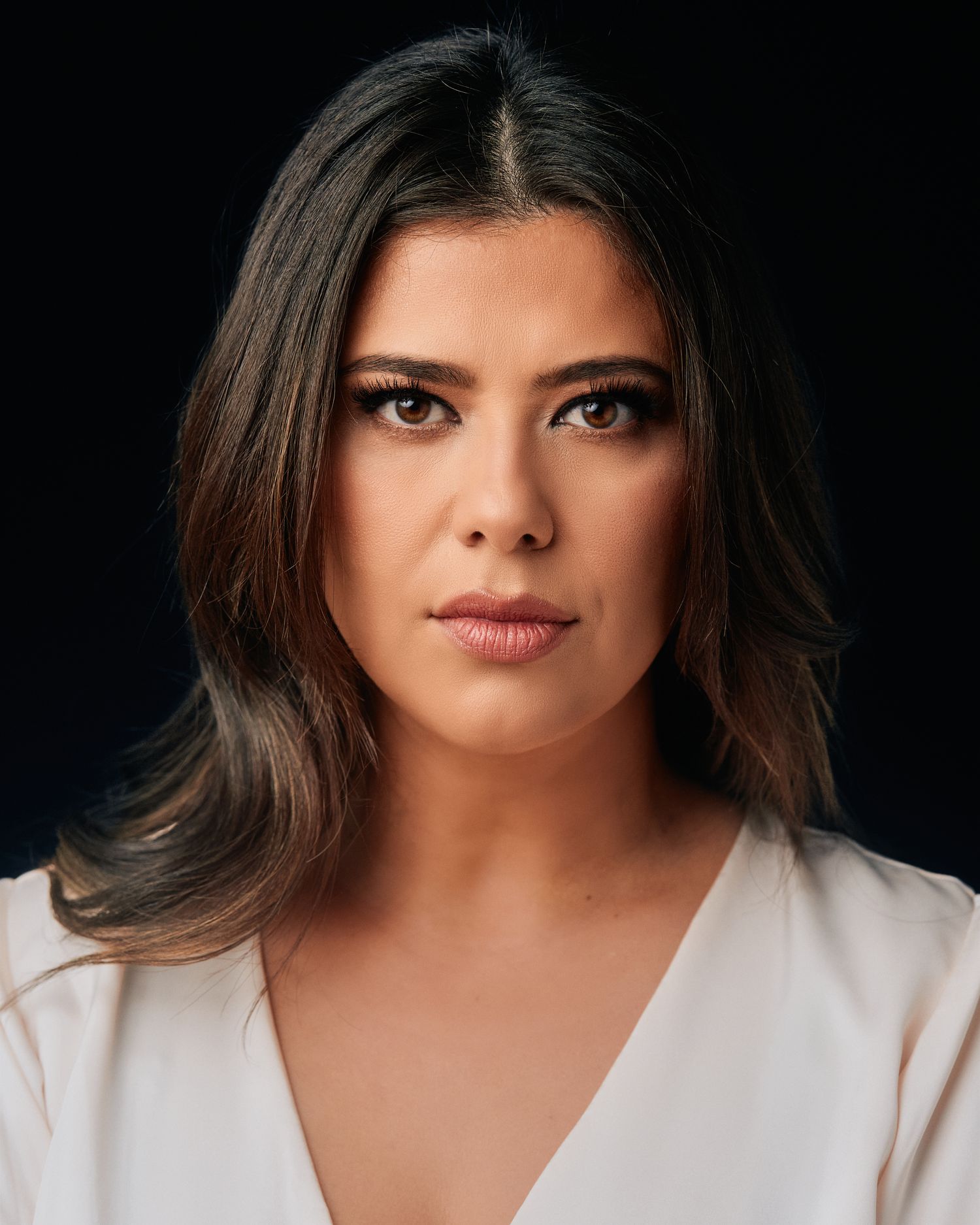 Professional studio portrait with dramatic lighting against dark background showcasing elegant pose and white attire.