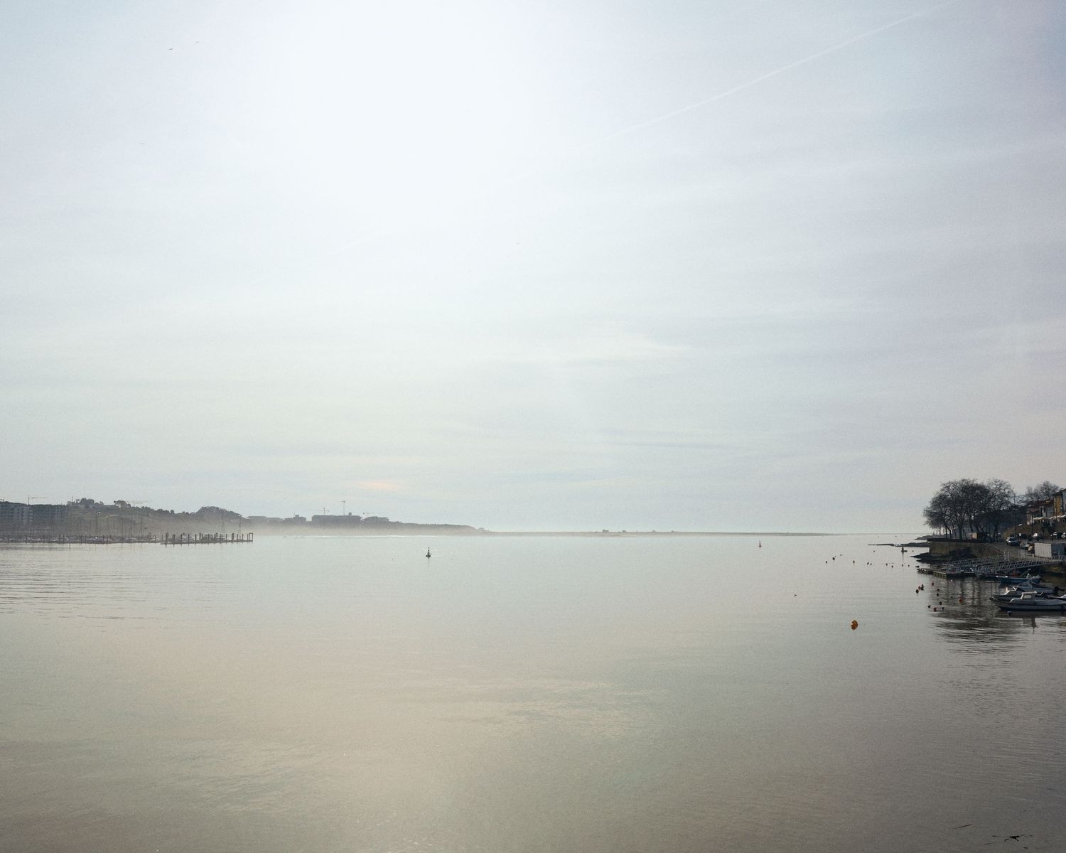 A serene panoramic view of a misty lake with calm waters stretching to the distant horizon.