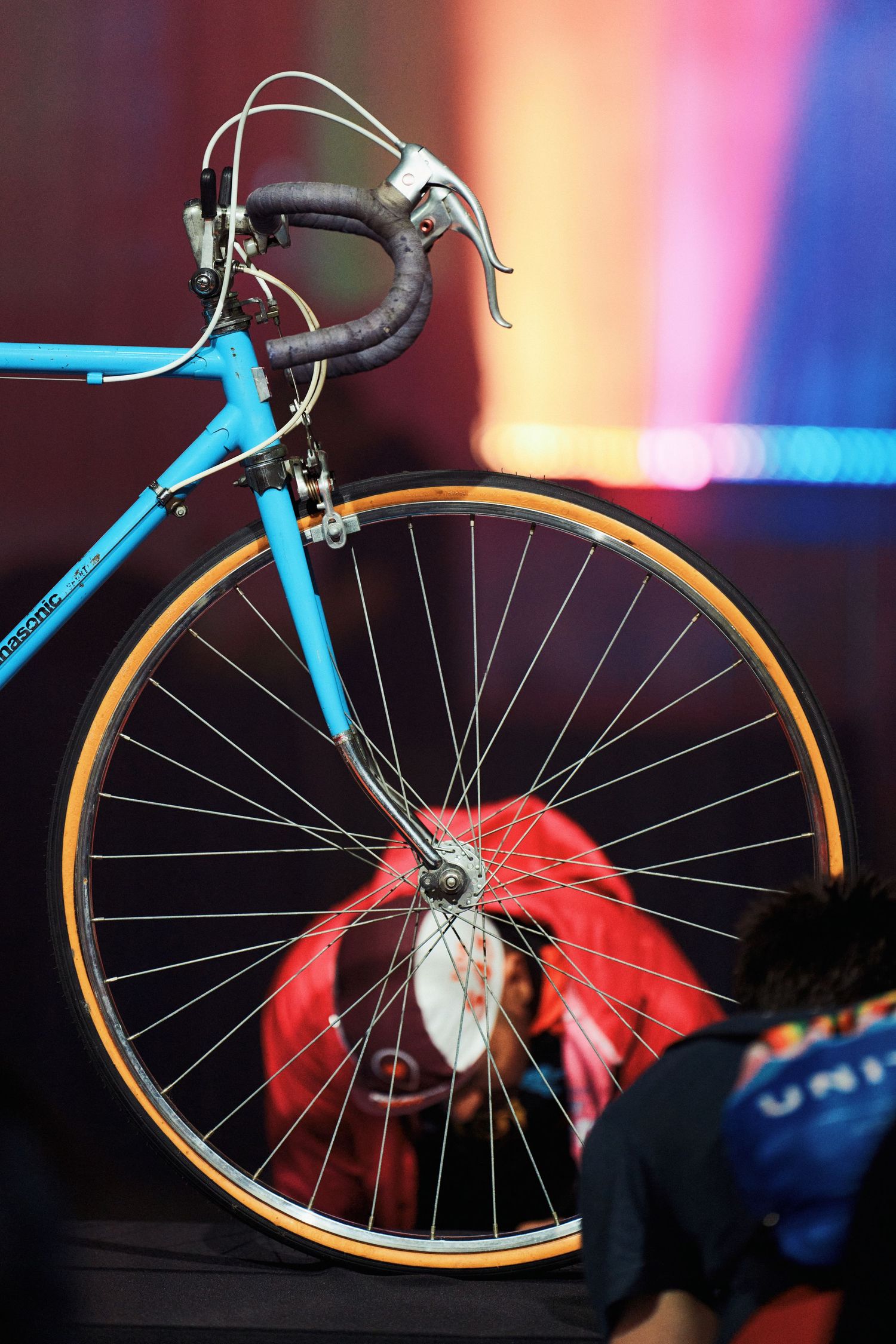 Turquoise vintage bicycle with drop handlebars and tan sidewall tires against colorful blurred background.