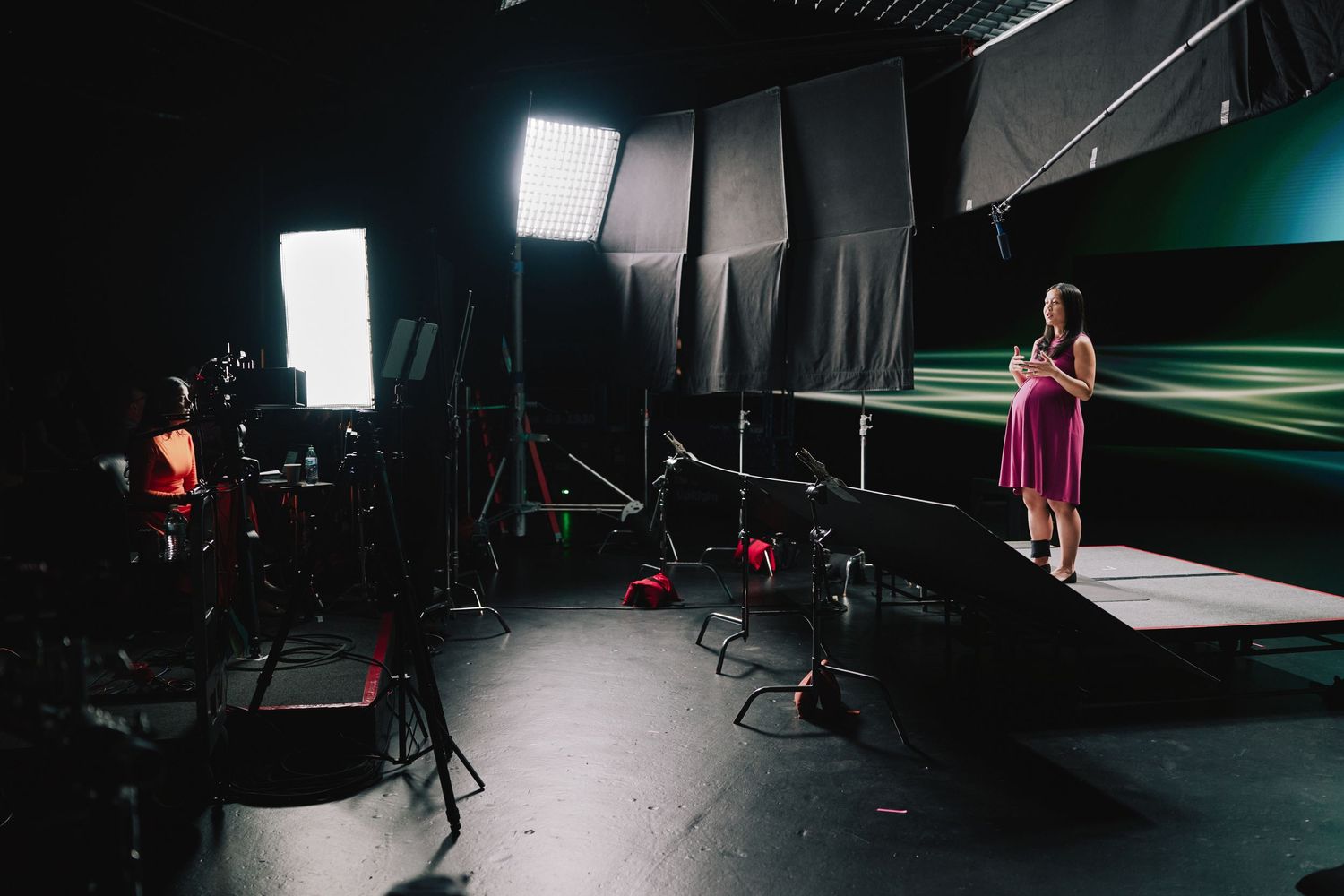 Behind the scenes studio setup with lighting equipment and a standing figure on a green screen stage.