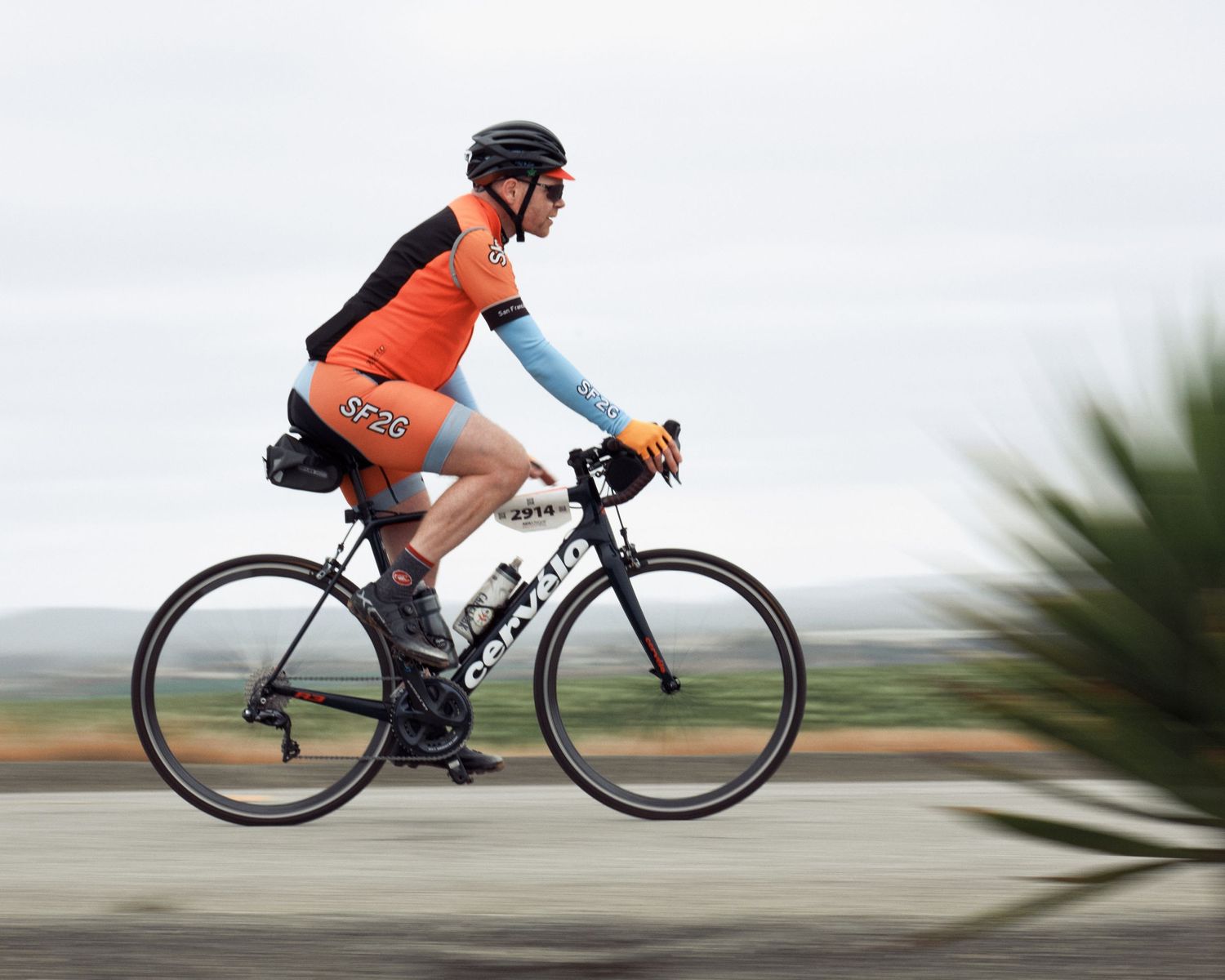 Side profile sequence of cyclist in orange racing down road showing dynamic motion and speed.