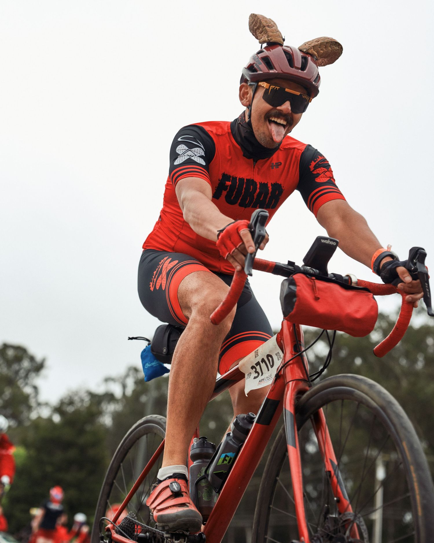 A cyclist in red attire and bunny ears rides a red road bike while wearing sunglasses.