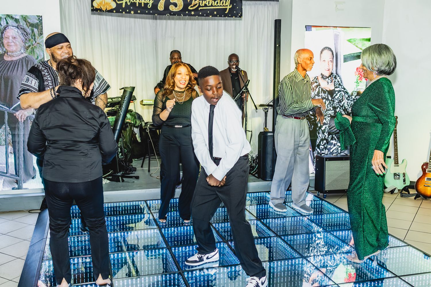People dancing and socializing at a 75th birthday party celebration with a live band performing in the background.