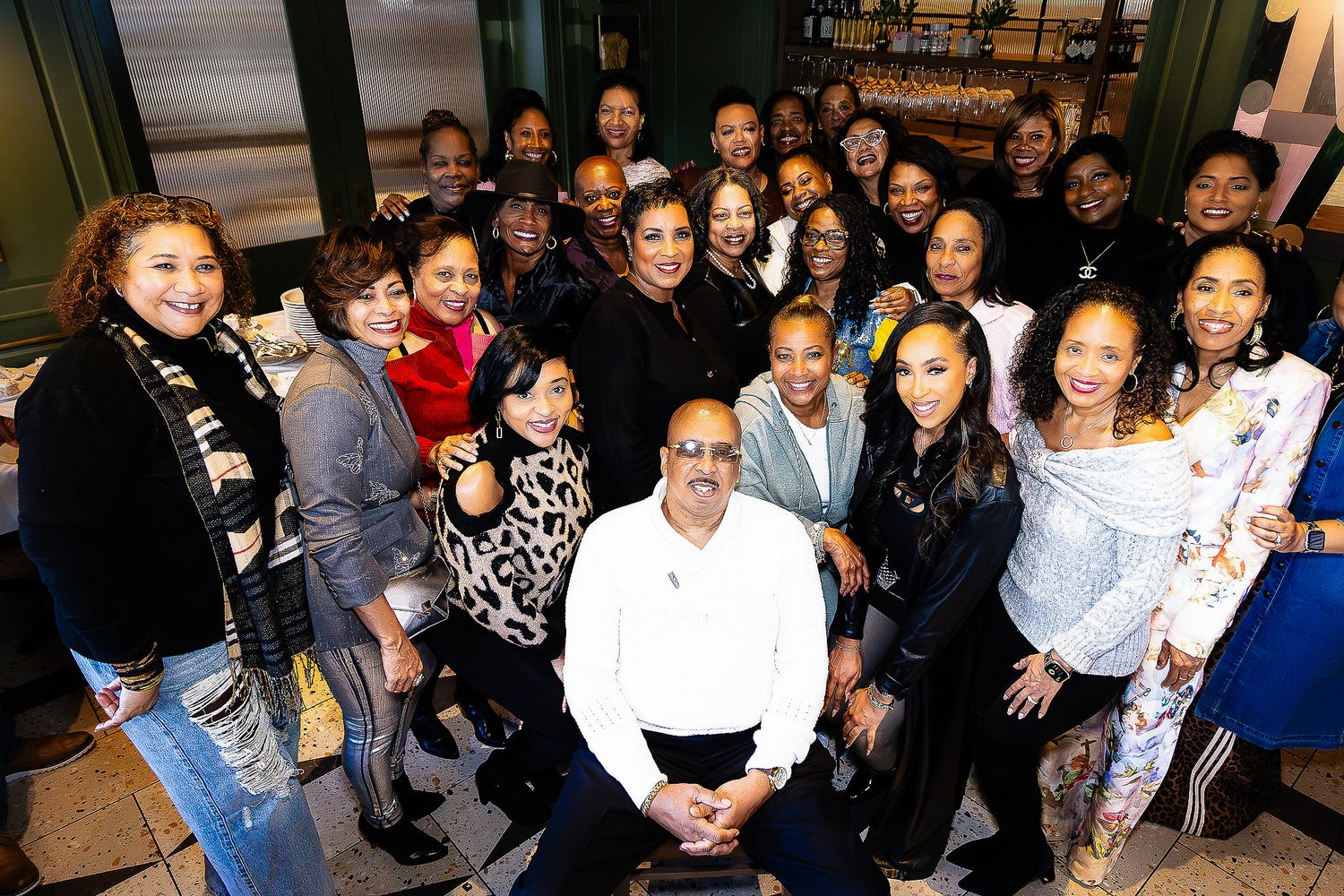 Large diverse group of smiling people posing together inside a restaurant, with one man seated in the center.