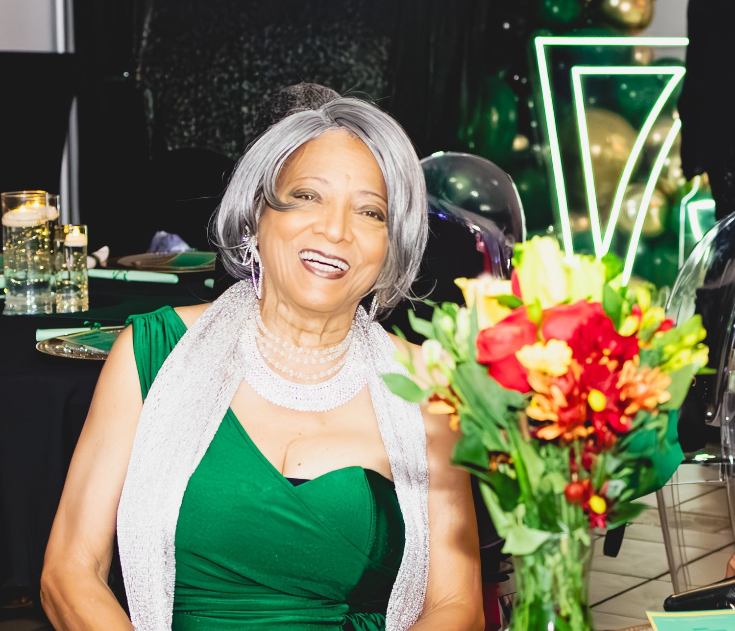 Someone in an elegant green dress and silver shawl poses with flowers at a formal event.