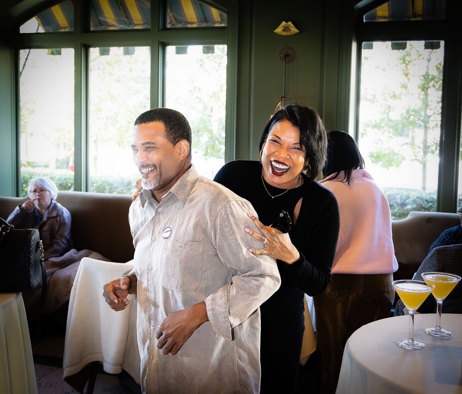 A man and woman laughing together in an elegant restaurant with cocktails on a nearby table.