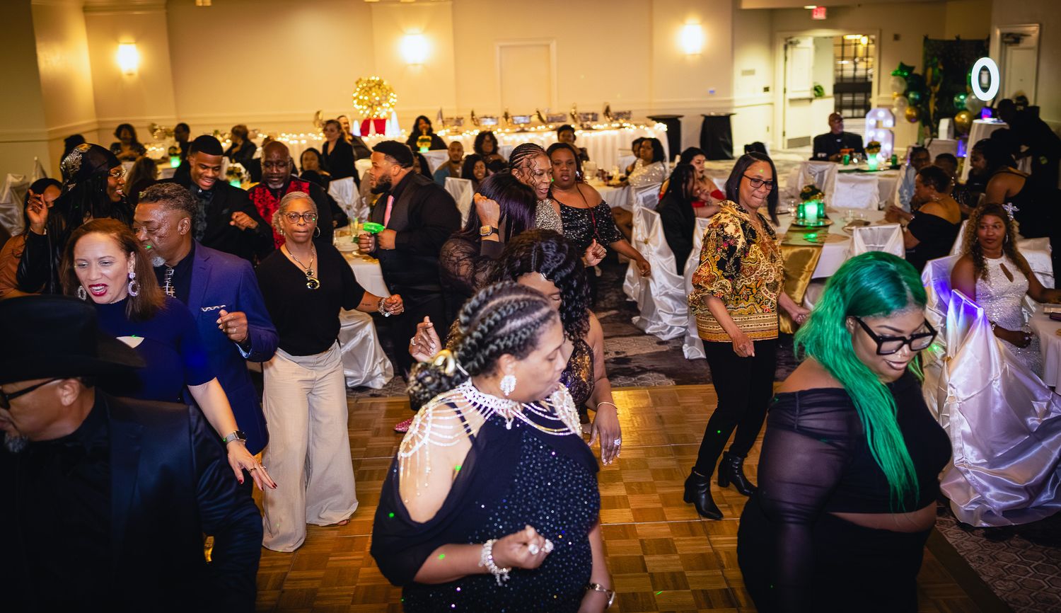 A lively indoor party with a large crowd of people dancing and celebrating in a decorated banquet hall.